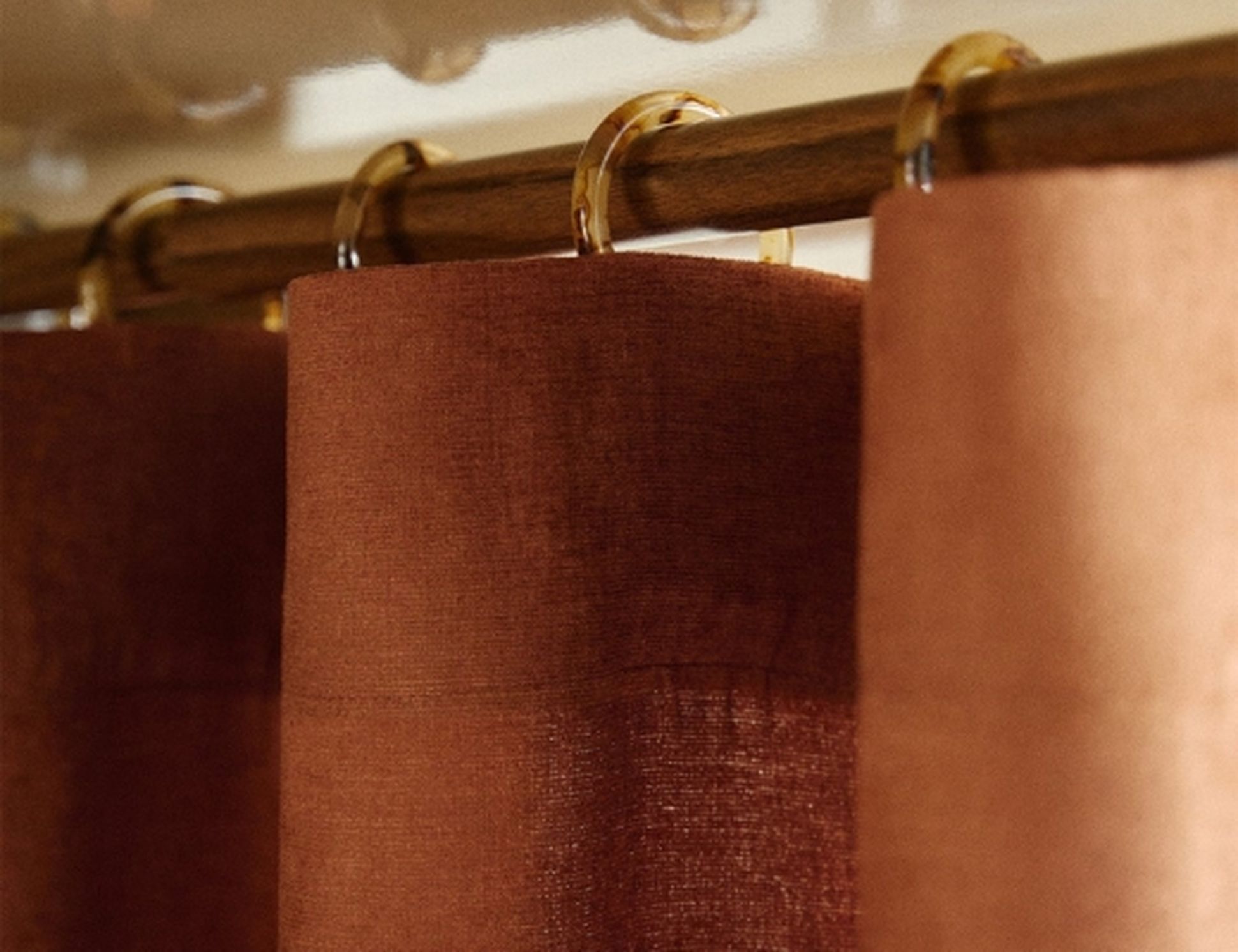 Gros plan sur des rideaux de douche marron suspendus à une tringle à l'aide d'anneaux ronds, mettant en valeur leur tissu texturé.
