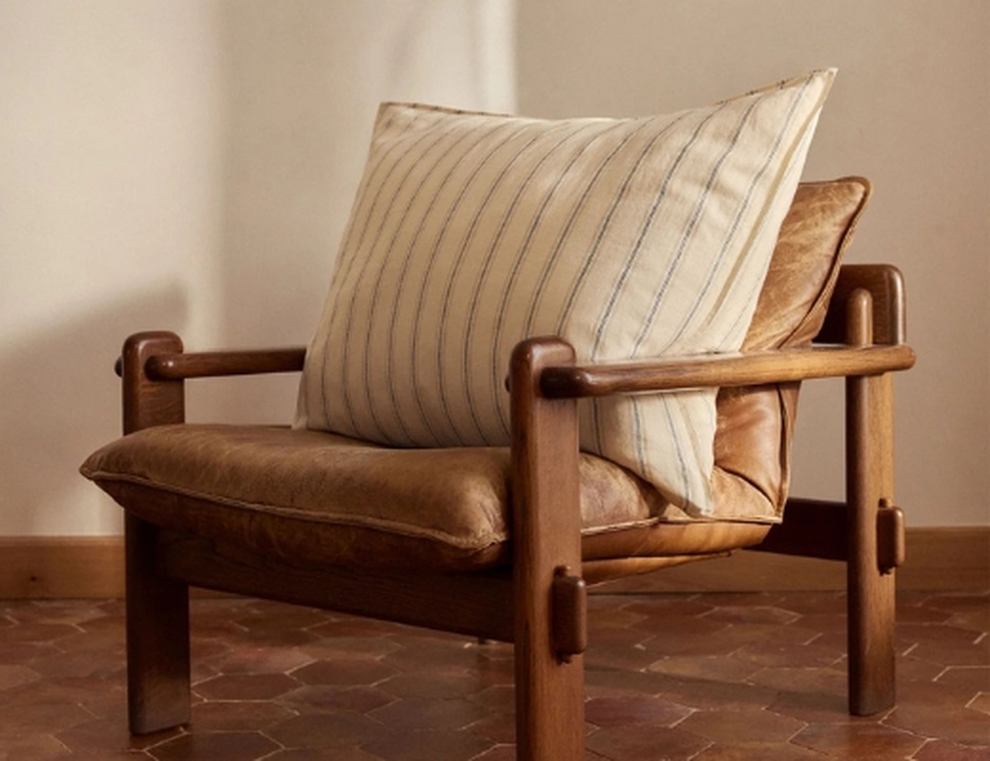 Une élégante chaise en bois avec des coussins en cuir et un coussin rayé, posée sur un sol carrelé dans une pièce chaleureuse.