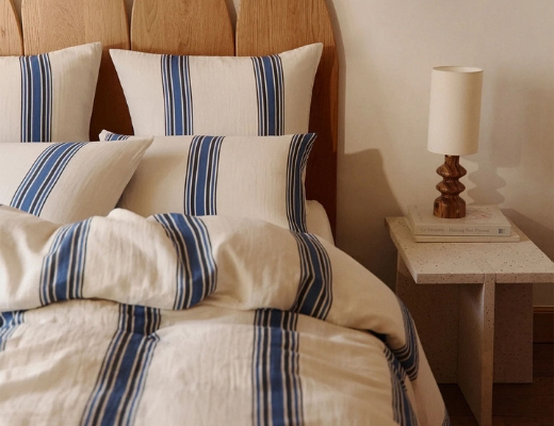 Un lit avec des oreillers et une couverture à rayures bleues, une tête de lit en bois et une table de chevet avec une lampe.