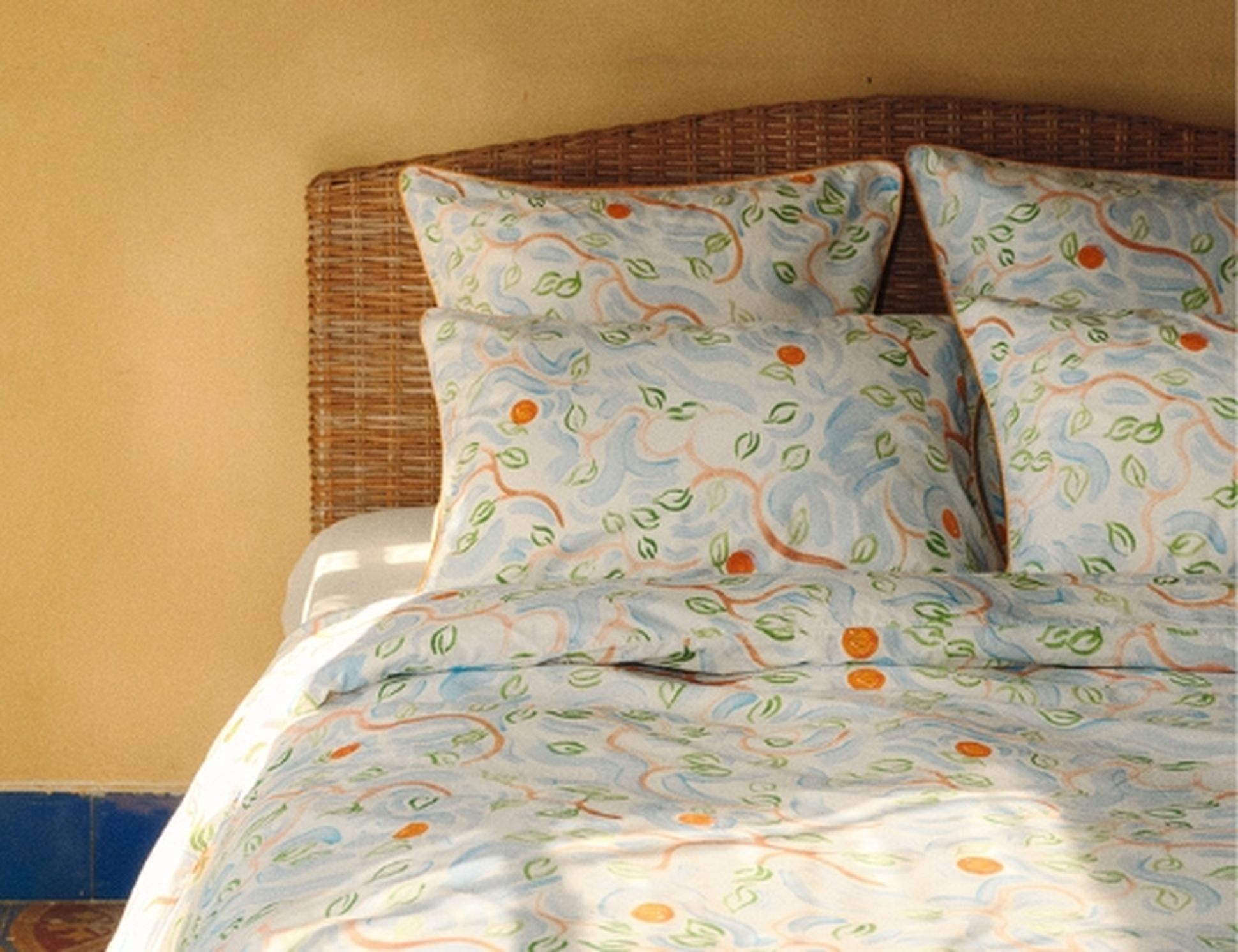 Lit douillet avec des oreillers et une couette bleu clair soigneusement disposés, une tête de lit en bois et une lampe beige dans une pièce faiblement éclairée.