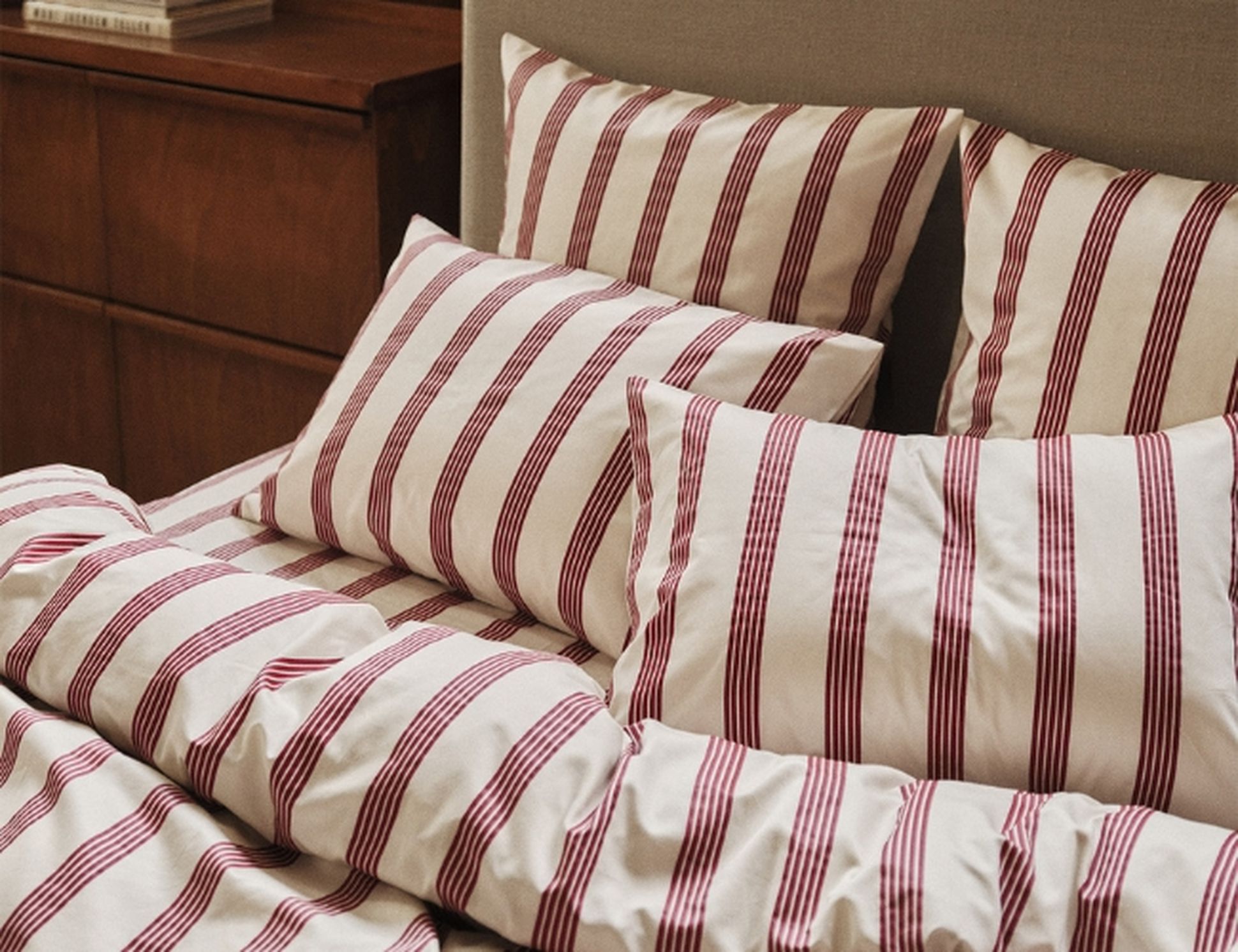 Linge de lit rayé de bordeaux et de blanc sur un lit agrémenté de plusieurs oreillers et d'une couette, dans une chambre à l'ambiance chaleureuse.