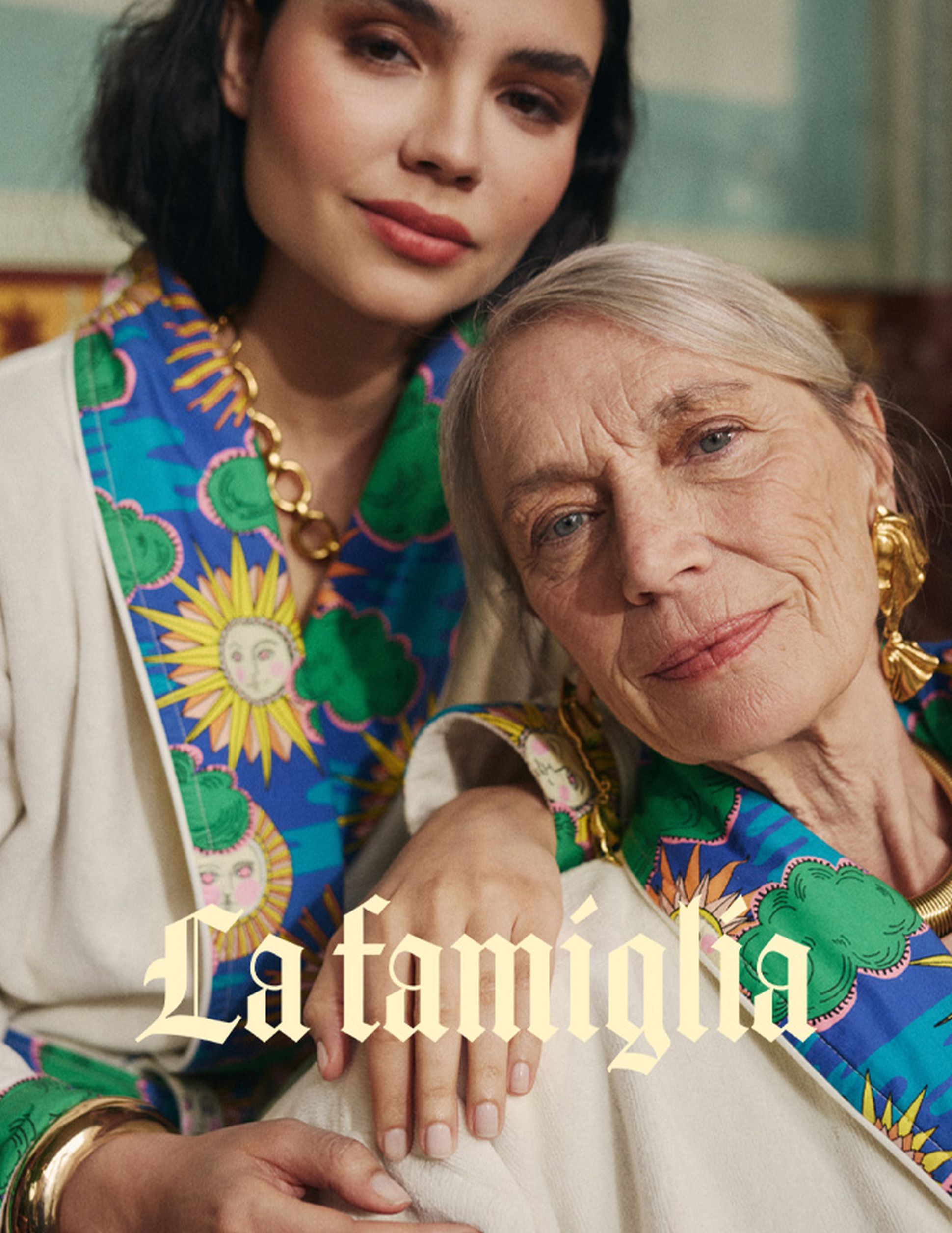 Deux femmes vêtues de peignoirs aux couleurs vives, ornés de motifs représentant le soleil et des nuages, posent côte à côte. Le texte « La famiglia » est superposé dans une police élégan