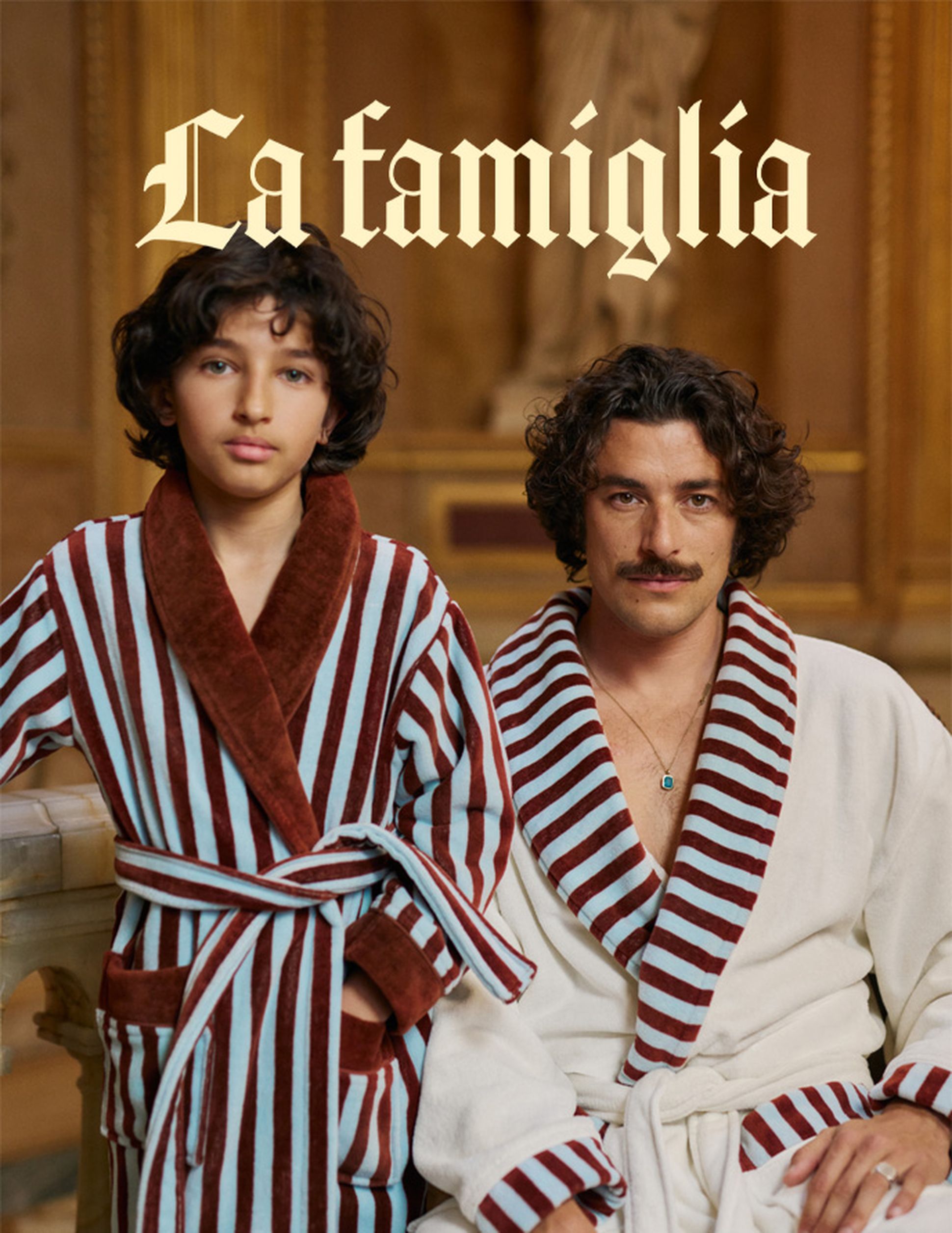 Deux personnes vêtues de peignoirs rayés posent à l'intérieur devant un décor somptueux. Le texte « La famiglia » apparaît au-dessus d'elles.