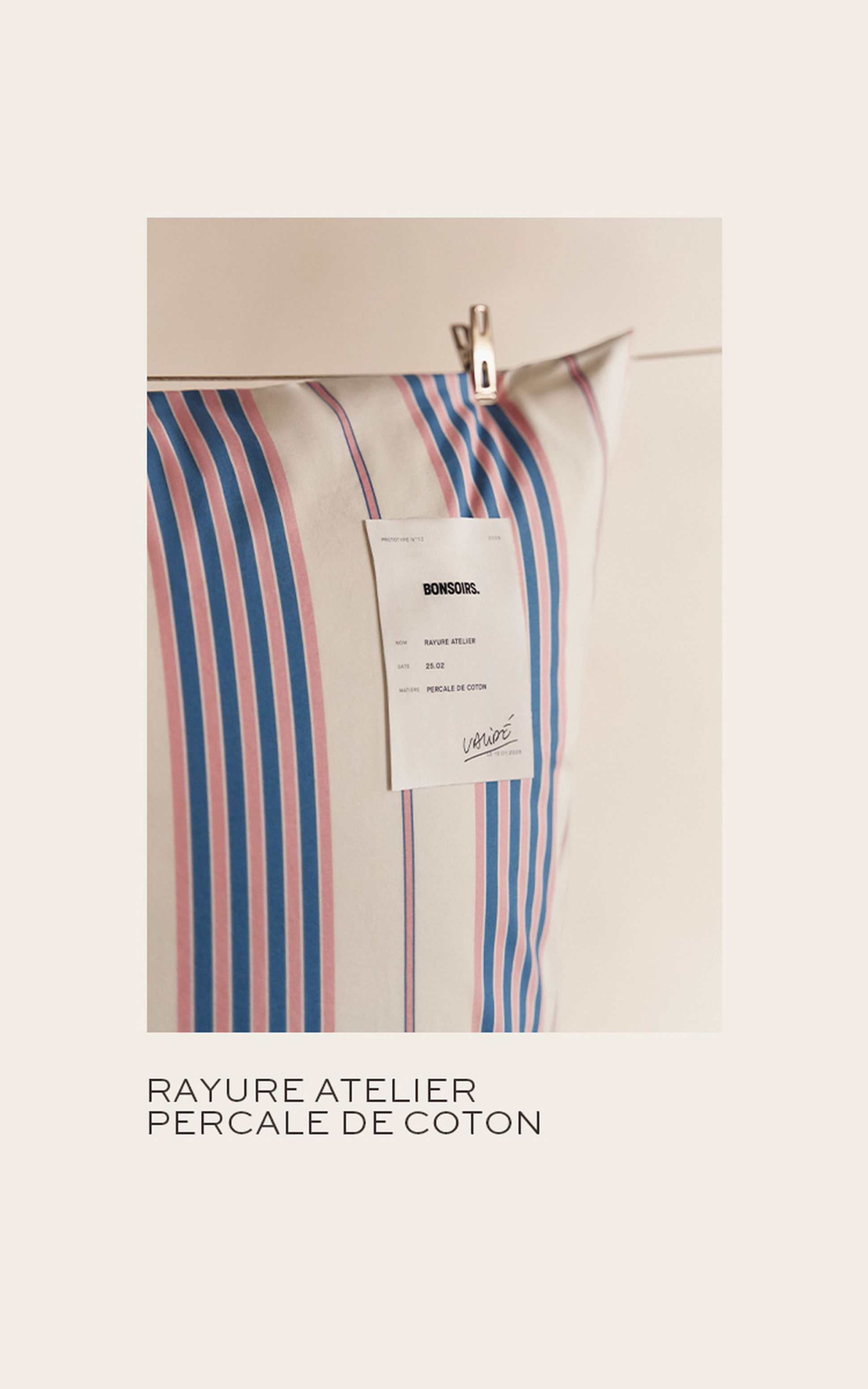 Un oreiller à rayures bleues et roses, orné d'une étiquette blanche portant l'inscription « BONSOIRS », est suspendu à un clip sur un fond clair.