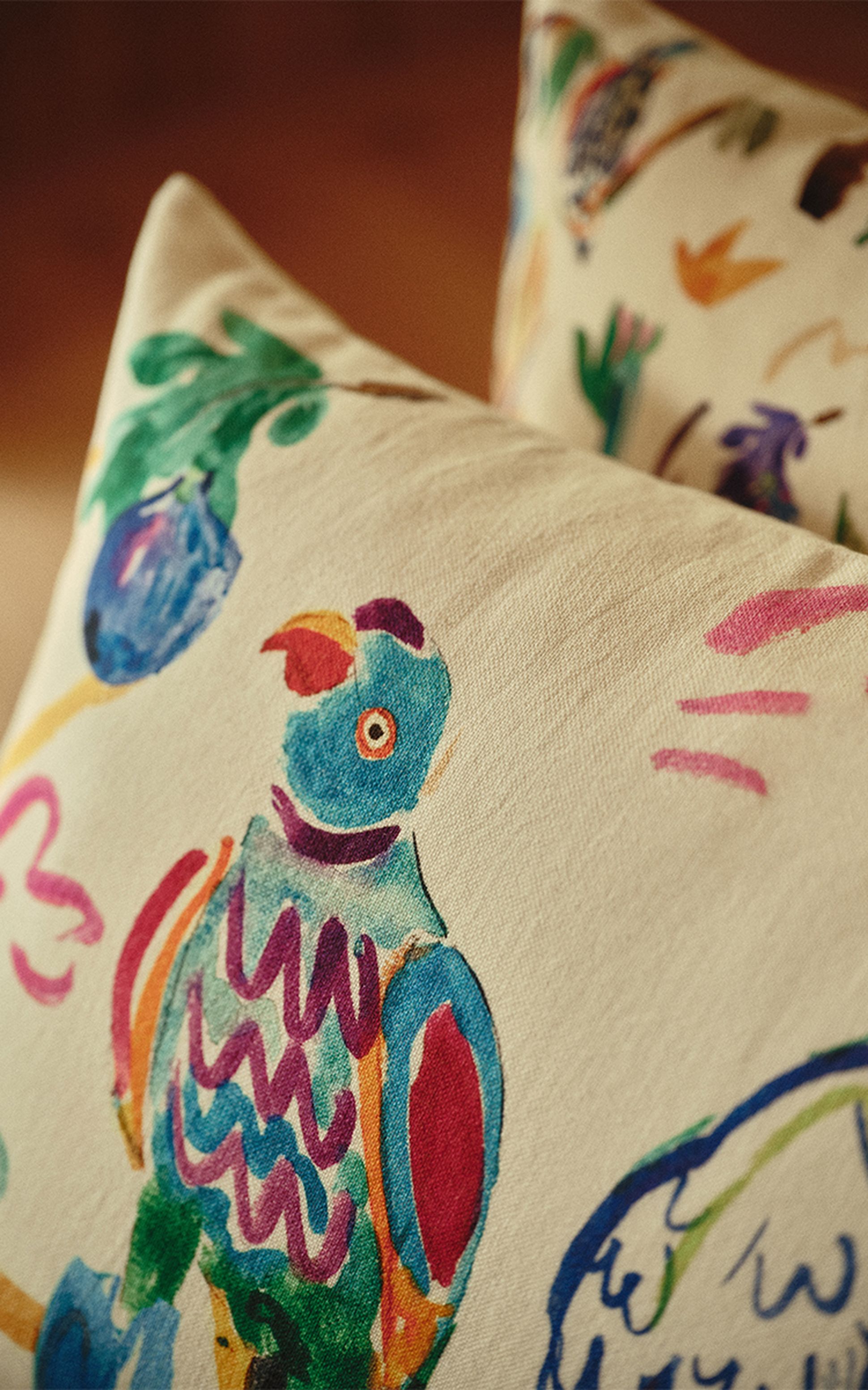 Gros plan sur un coussin beige orné d'un motif abstrait et coloré représentant un perroquet, dans des tons de bleu, de vert et de rouge, sur un fond flou.