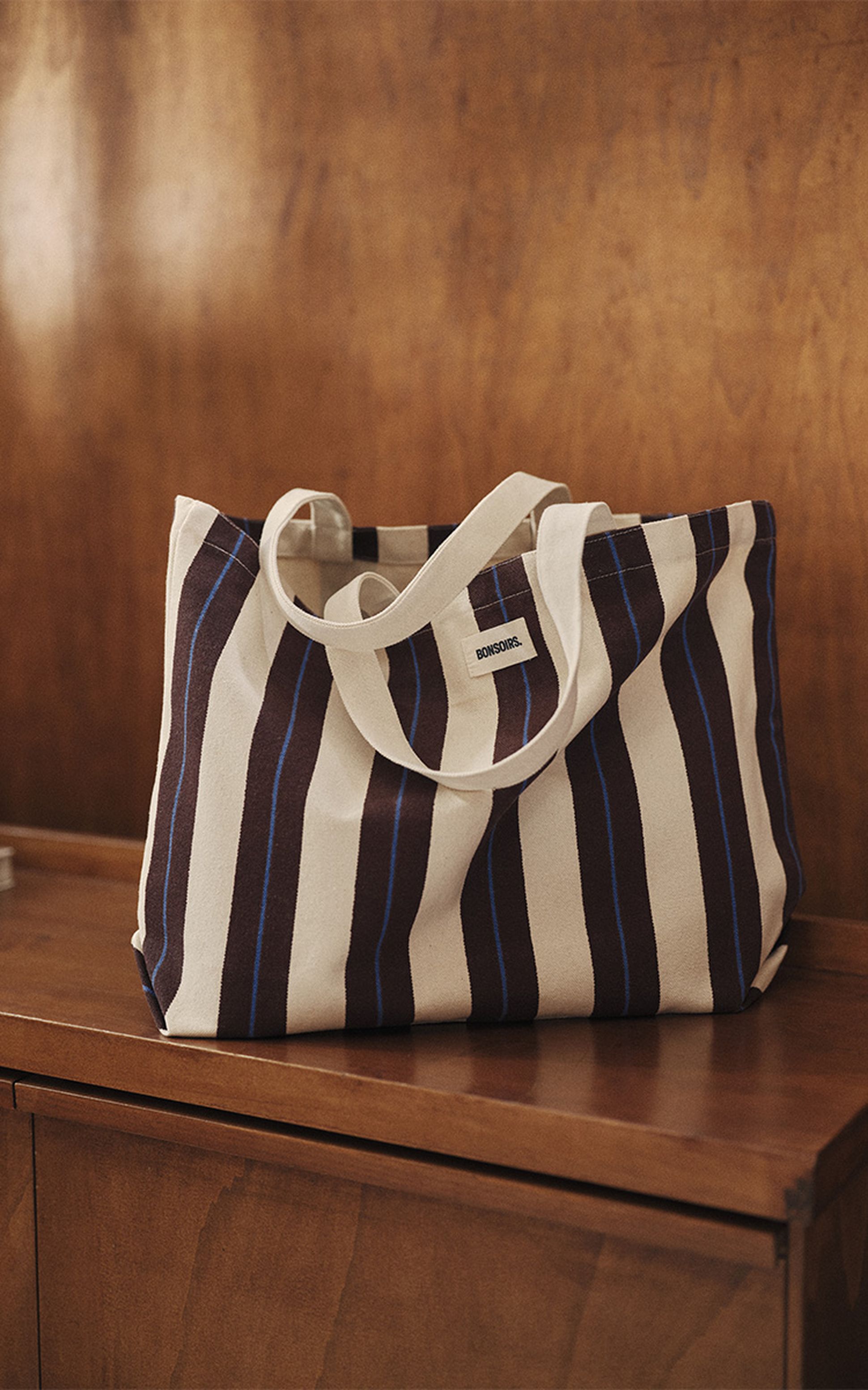 Un sac fourre-tout en toile à rayures verticales claires et foncées repose sur une surface en bois.