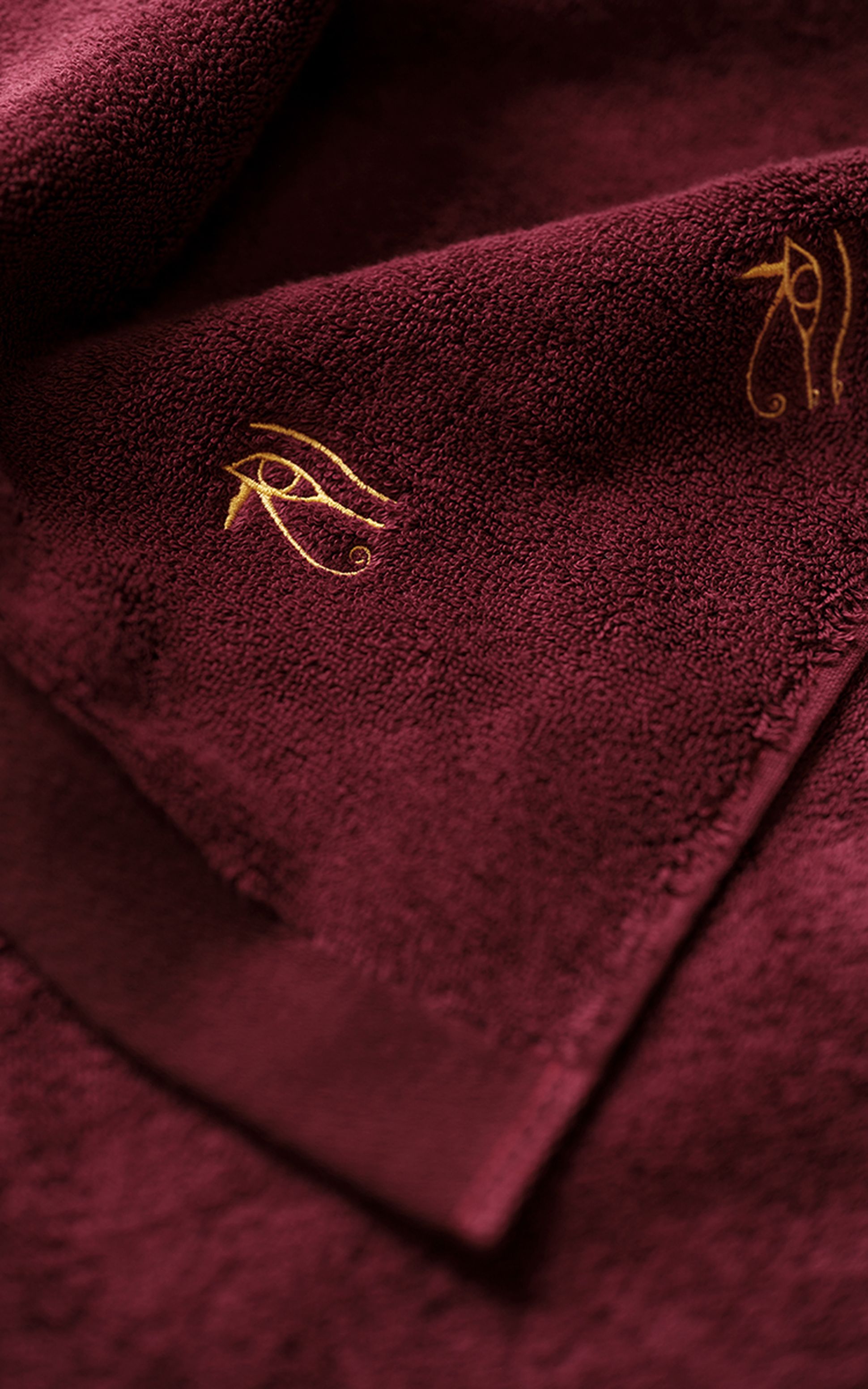 A dark red towel with a golden embroidered Eye of Horus symbol on the fabric.