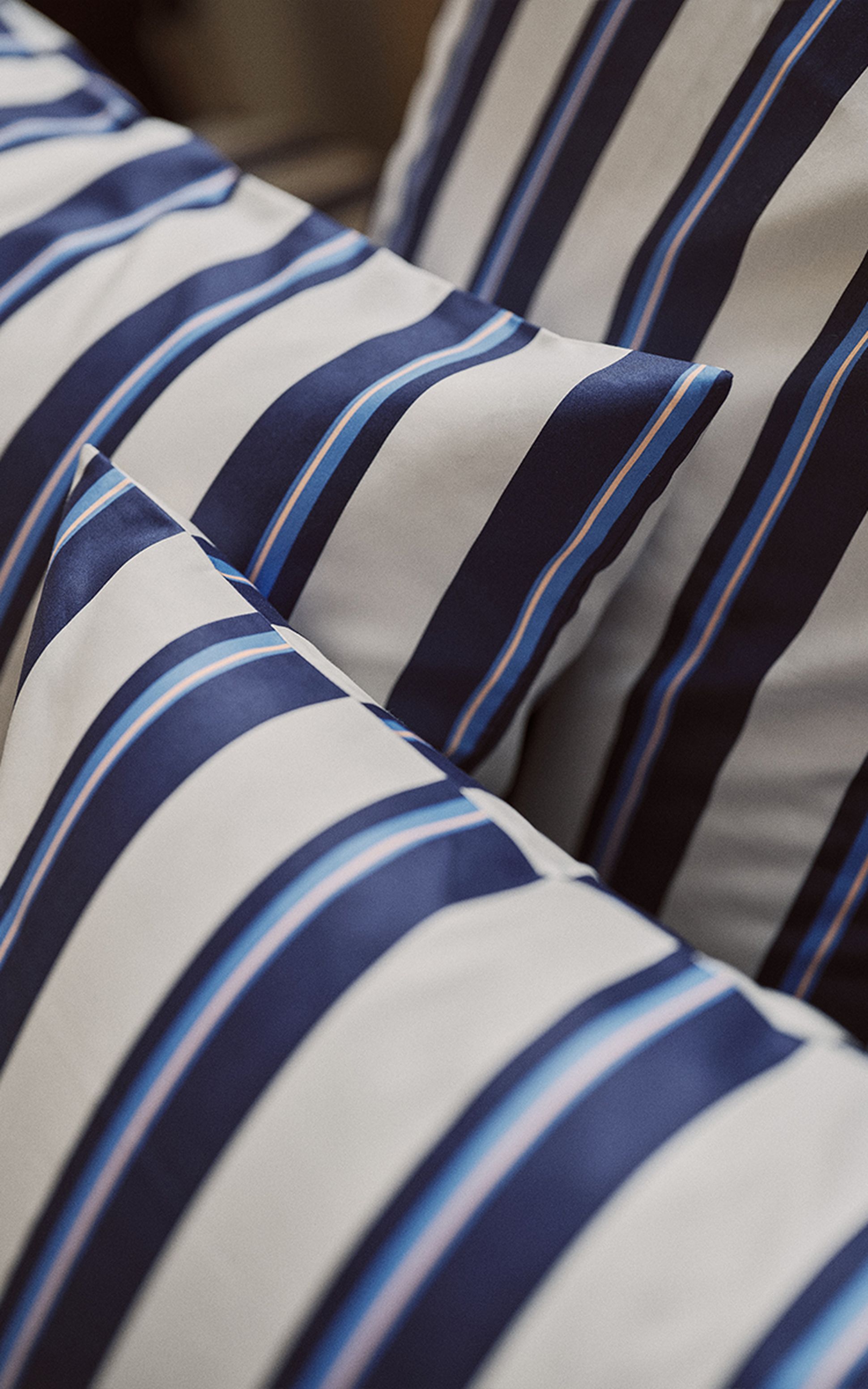 Gros plan sur des coussins à rayures bleues, blanches et bleu clair. Le tissu semble lisse et les rayures sont en diagonale.