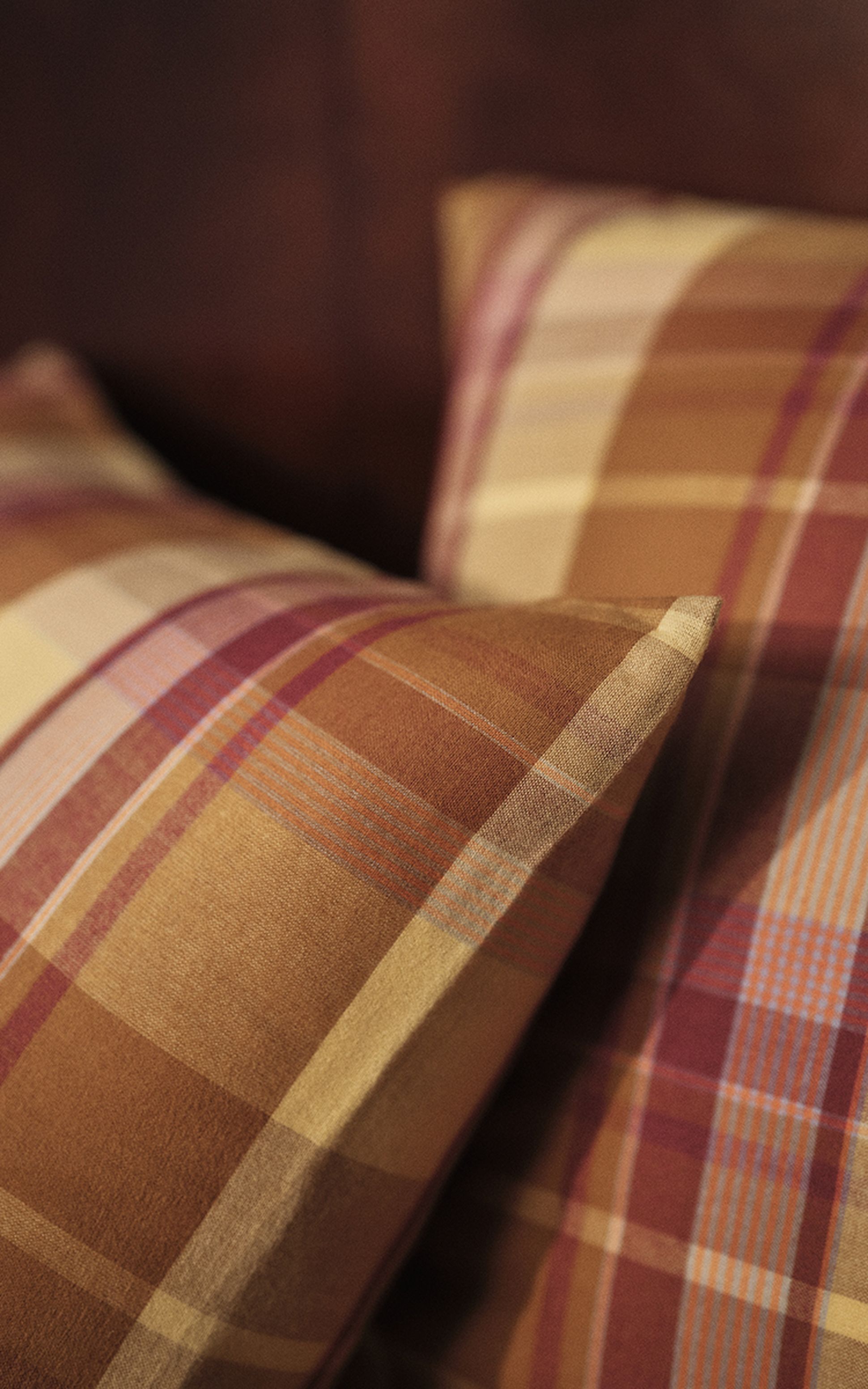 Gros plan sur deux coussins à carreaux aux teintes chaudes – nuances de marron, de rouge et de beige –, disposés avec soin.