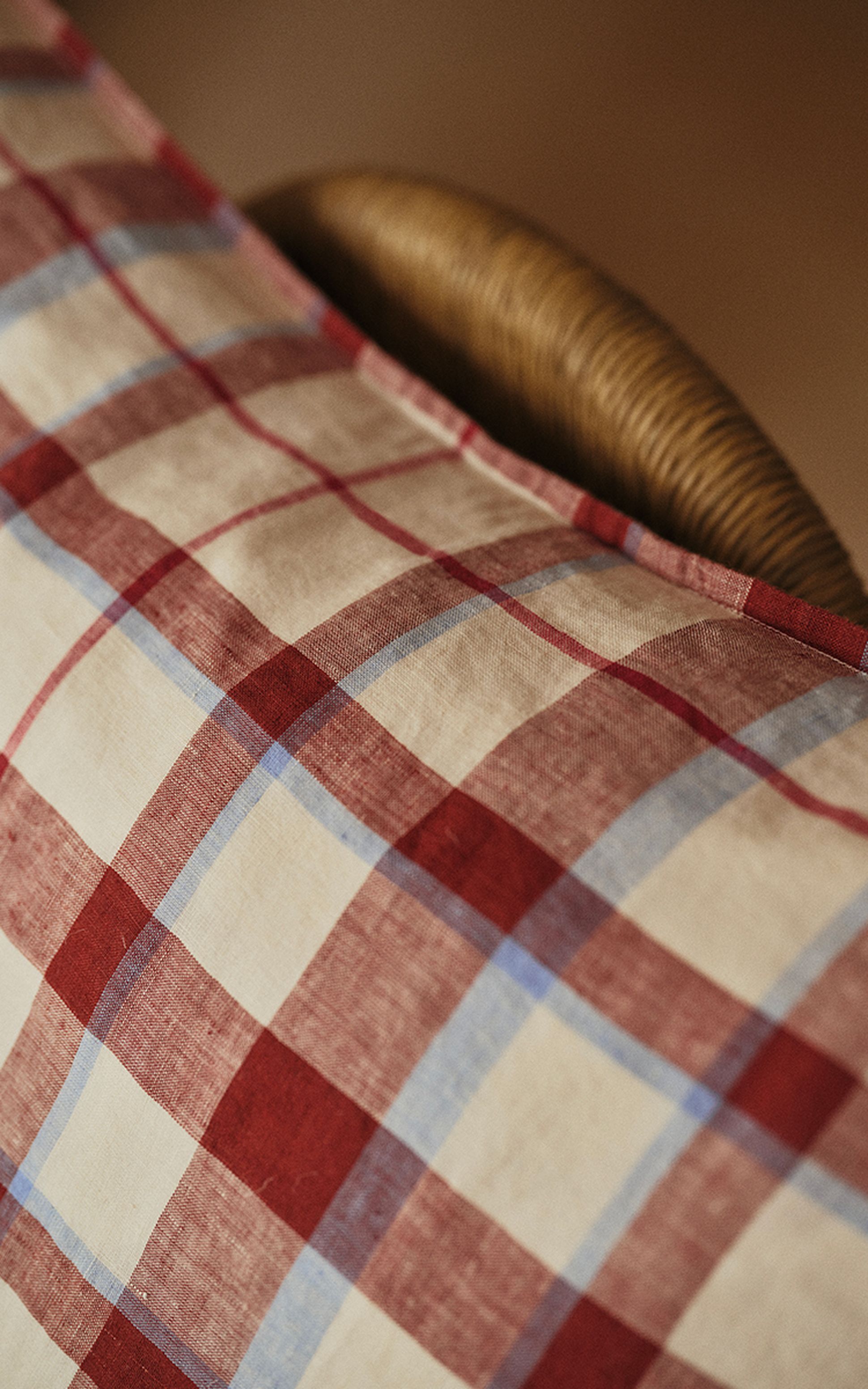 Gros plan sur un tissu à carreaux rouges, blancs et bleus drapé sur une chaise en osier, créant une ambiance chaleureuse et rustique.