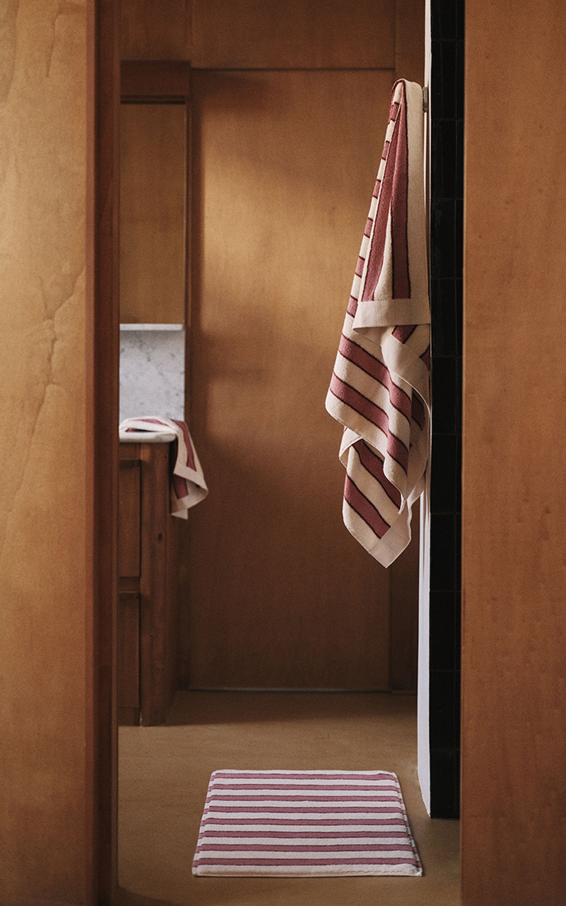 Salle de bains lambrissée, agrémentée d'un tapis et d'une serviette à rayures. Une serviette à rayures assortie est suspendue à la porte, créant ainsi une ambiance chaleureuse et accueillante.