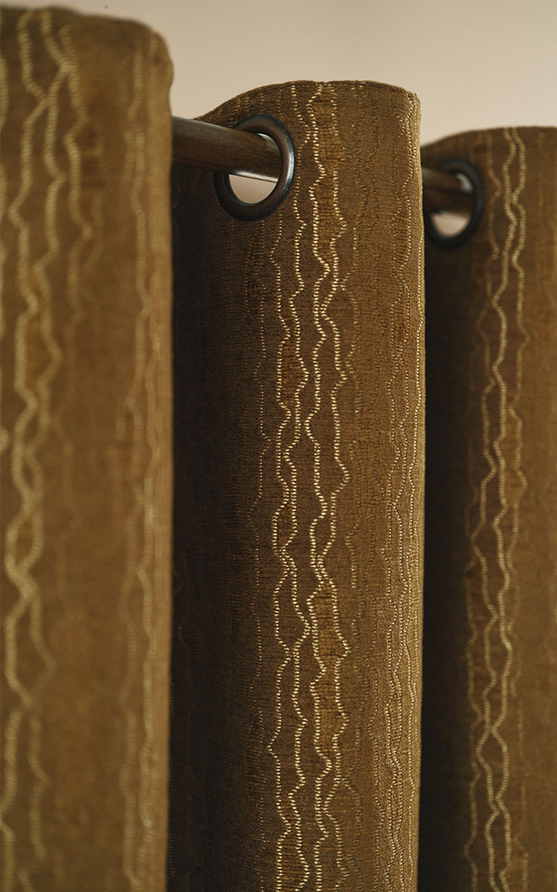 Brown curtain with wavy gold patterns, hanging from a rod using metal grommets, viewed up close.