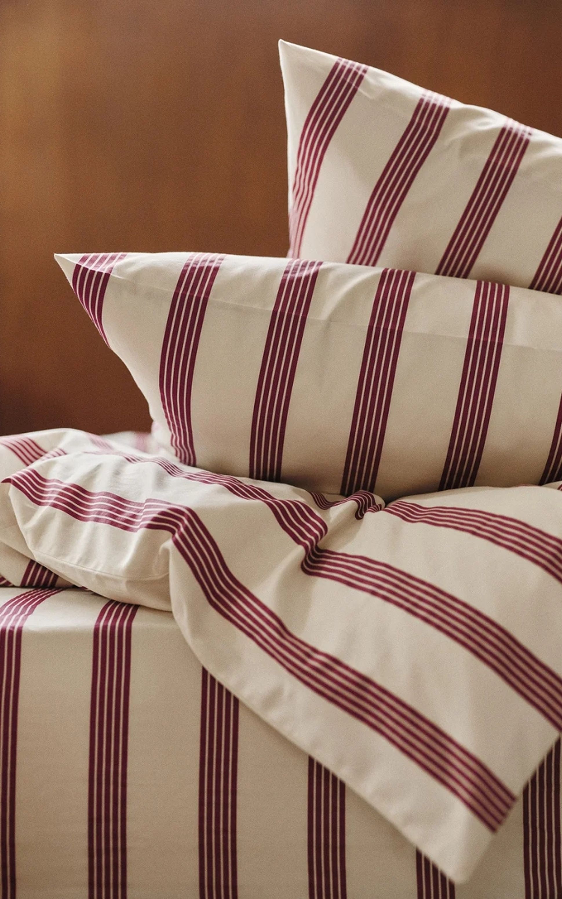 Un lit recouvert de draps couleur crème ornés de larges rayures verticales rouges, soigneusement arrangé avec deux oreillers assortis.