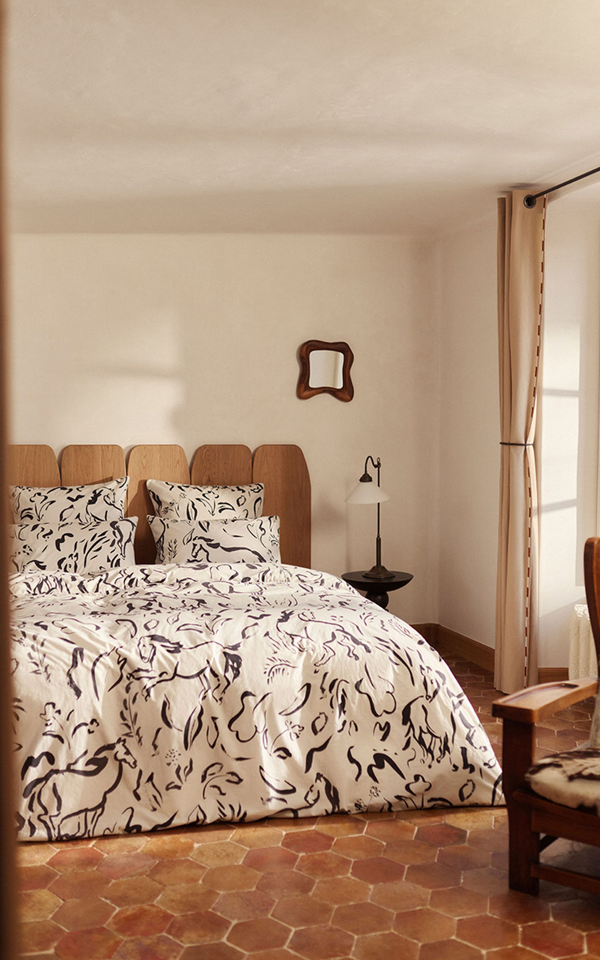 Chambre confortable avec un lit double recouvert de draps à motifs, une tête de lit en bois, un petit miroir et une lampe de chevet. Sol carrelé et éclairage tamisé.
