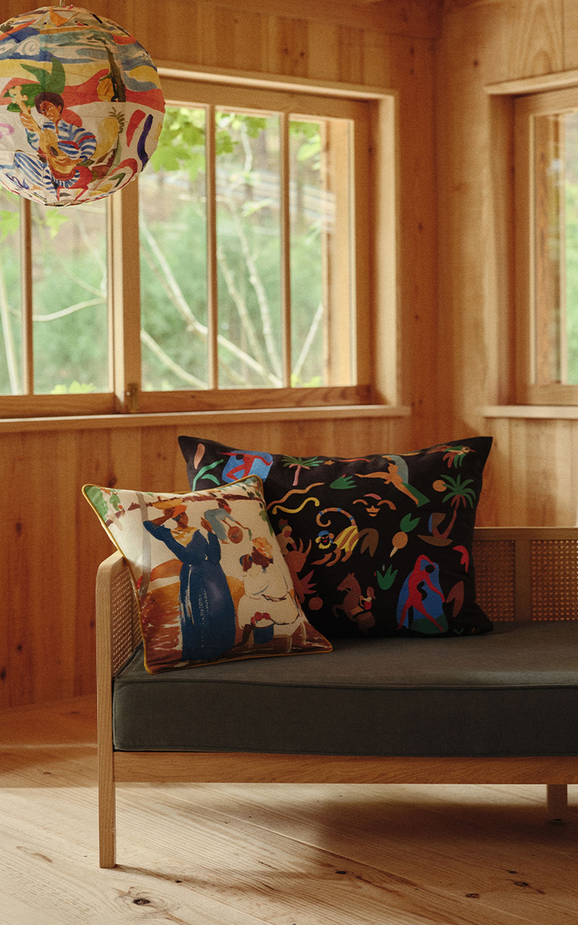 Une chambre chaleureuse en bois, avec un canapé, des coussins aux motifs colorés et une lanterne en papier aux couleurs vives près de la fenêtre.