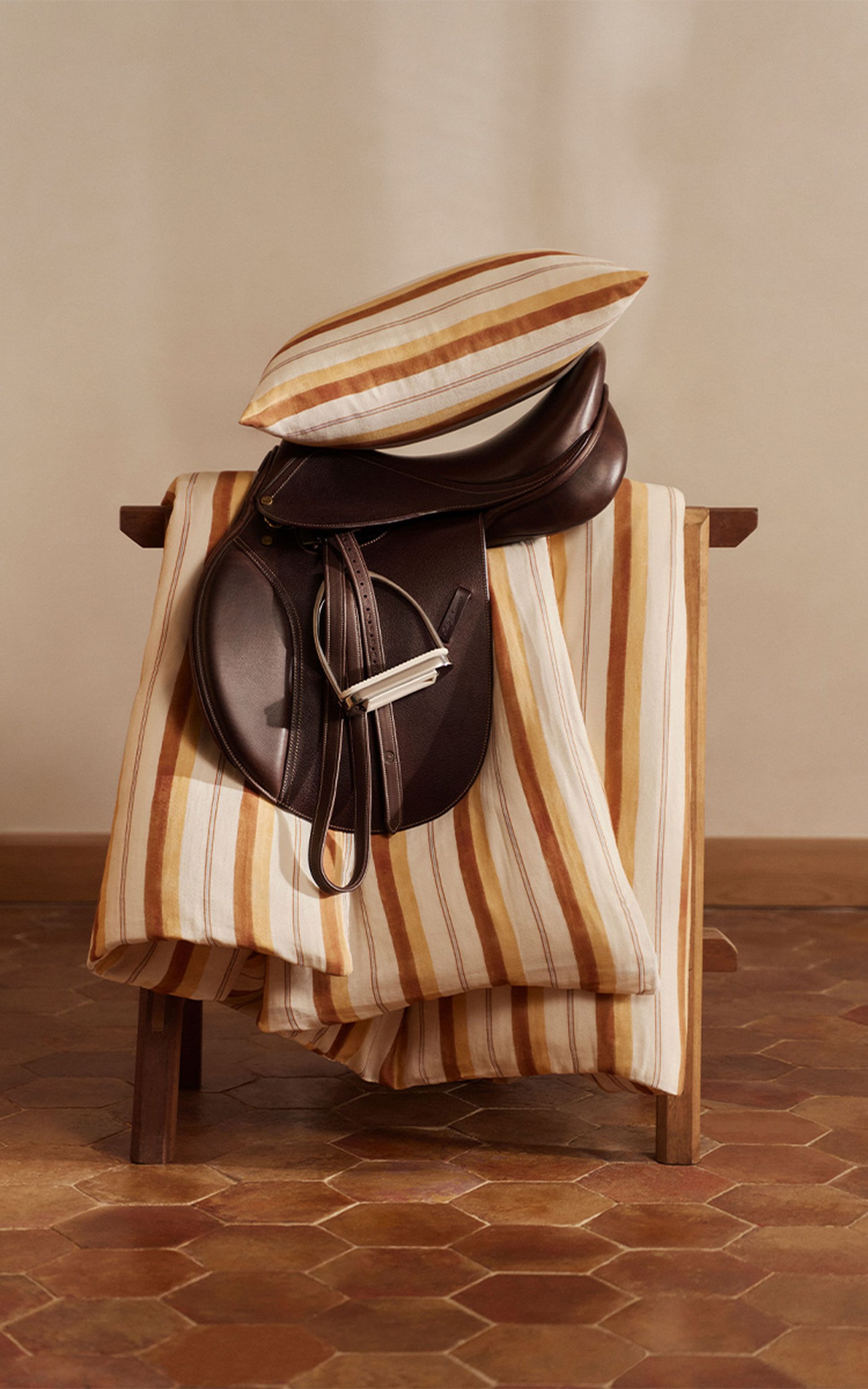 Une chaise en bois recouverte d'un tissu rayé et d'une selle en cuir foncé, surmontée d'un coussin rayé, posée sur un sol carrelé.