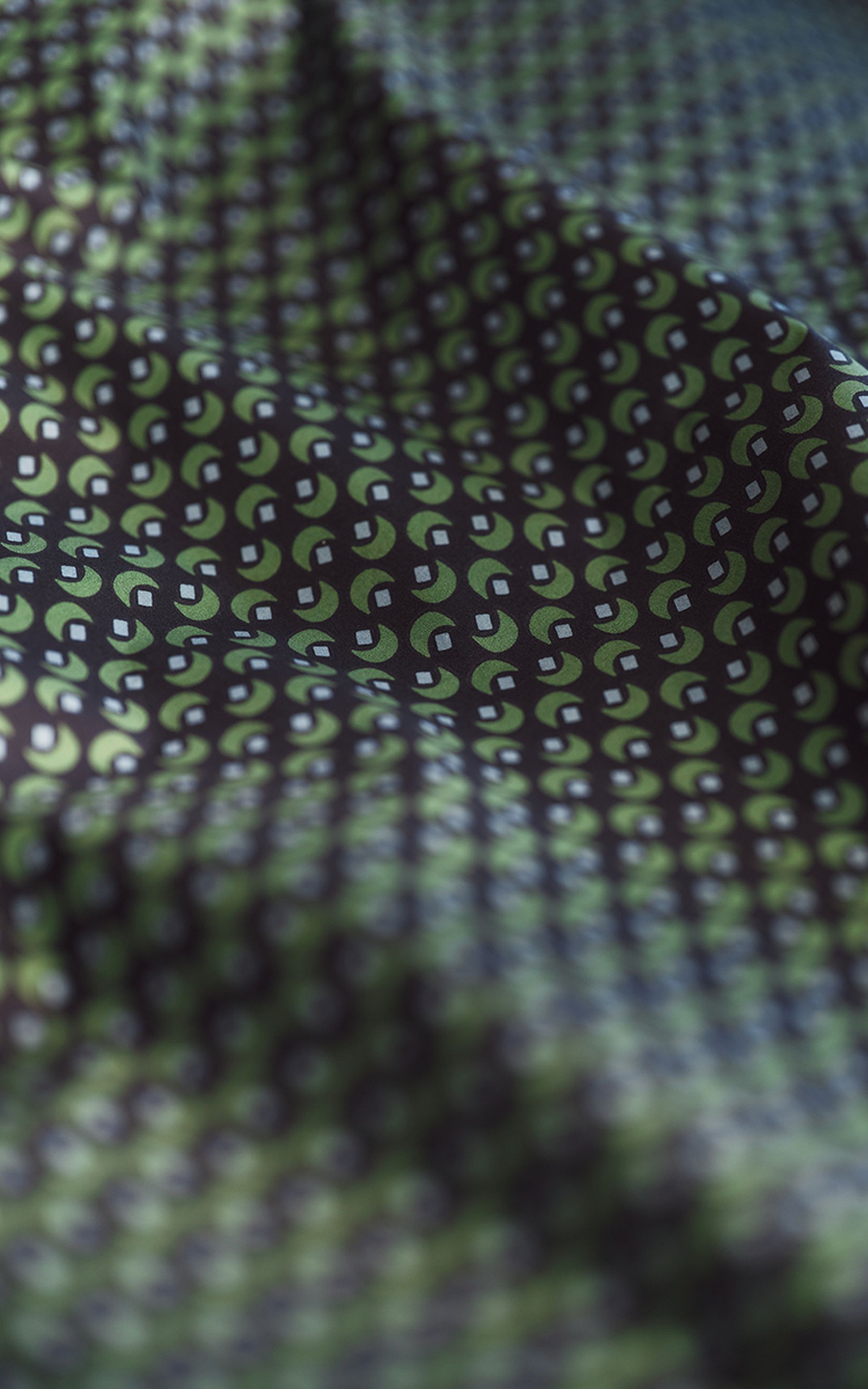 Close-up of a patterned fabric with green, black, and white geometric shapes creating a repeating design on a textured surface.