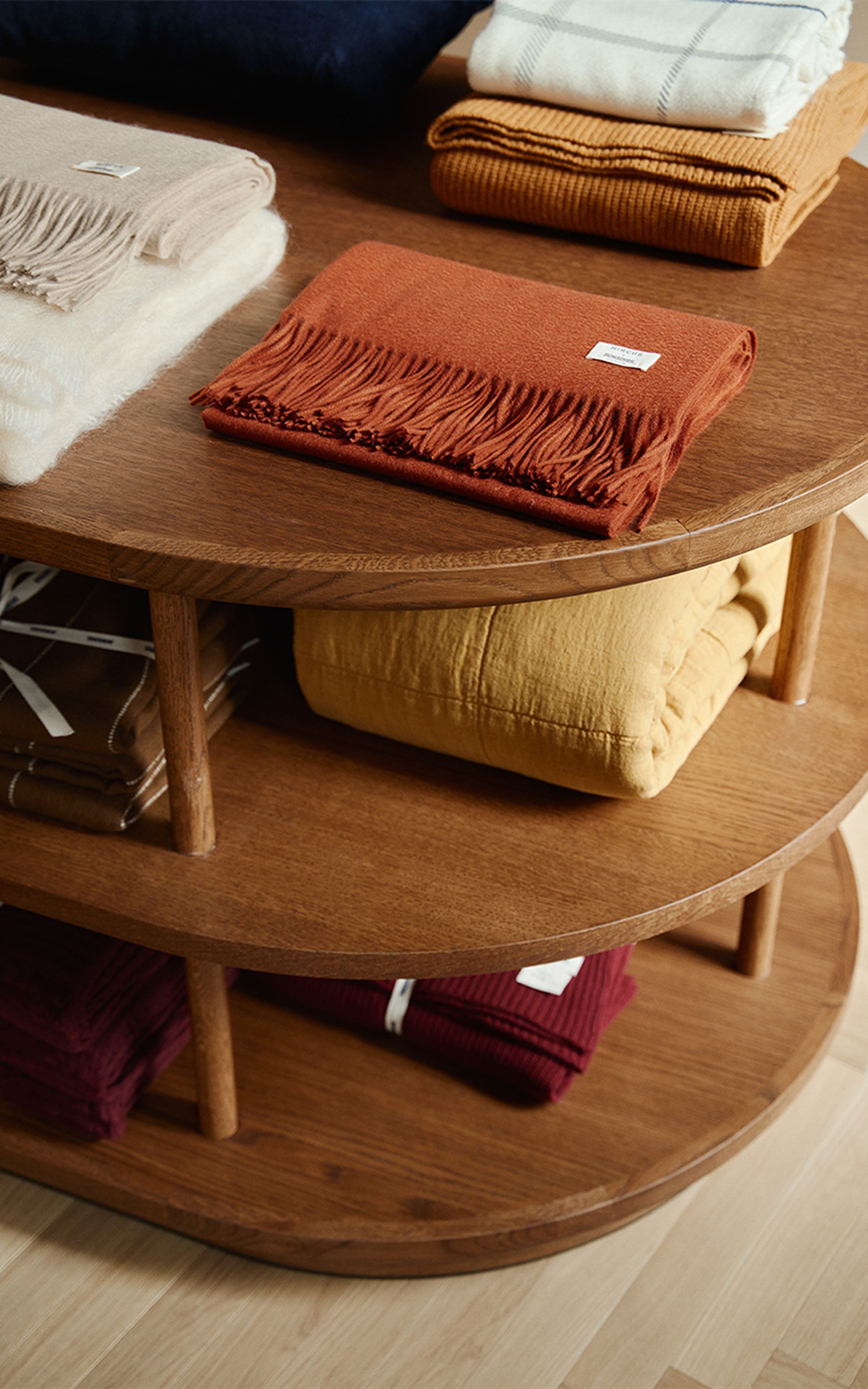 Une table de présentation en bois sur laquelle sont disposés, soigneusement pliés, des foulards et des couvertures colorés dans un magasin.