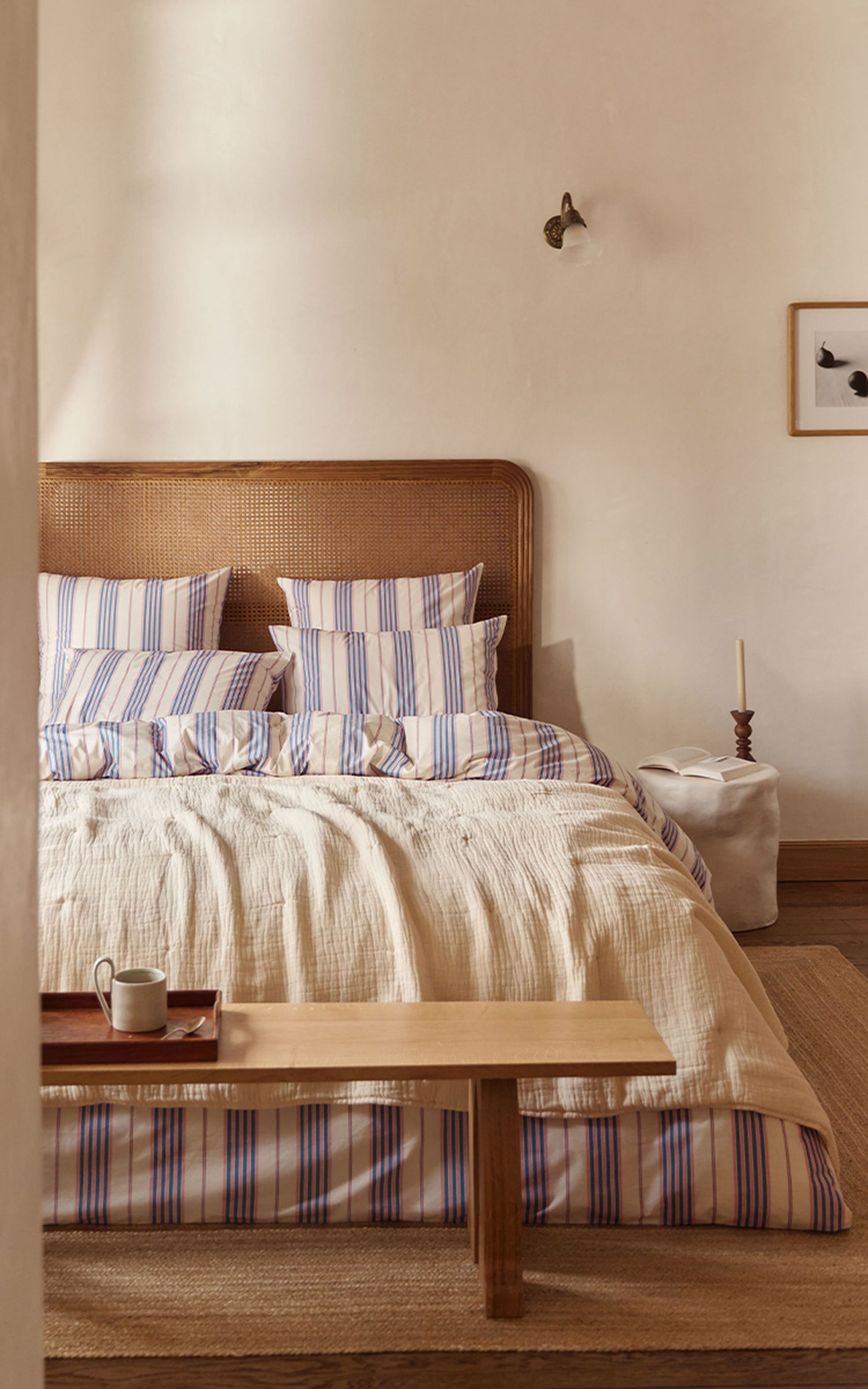 Chambre confortable avec une tête de lit en bois, une literie rayée, un banc en bois, un grand lampadaire, un petit tableau encadré et un tapis tissé.