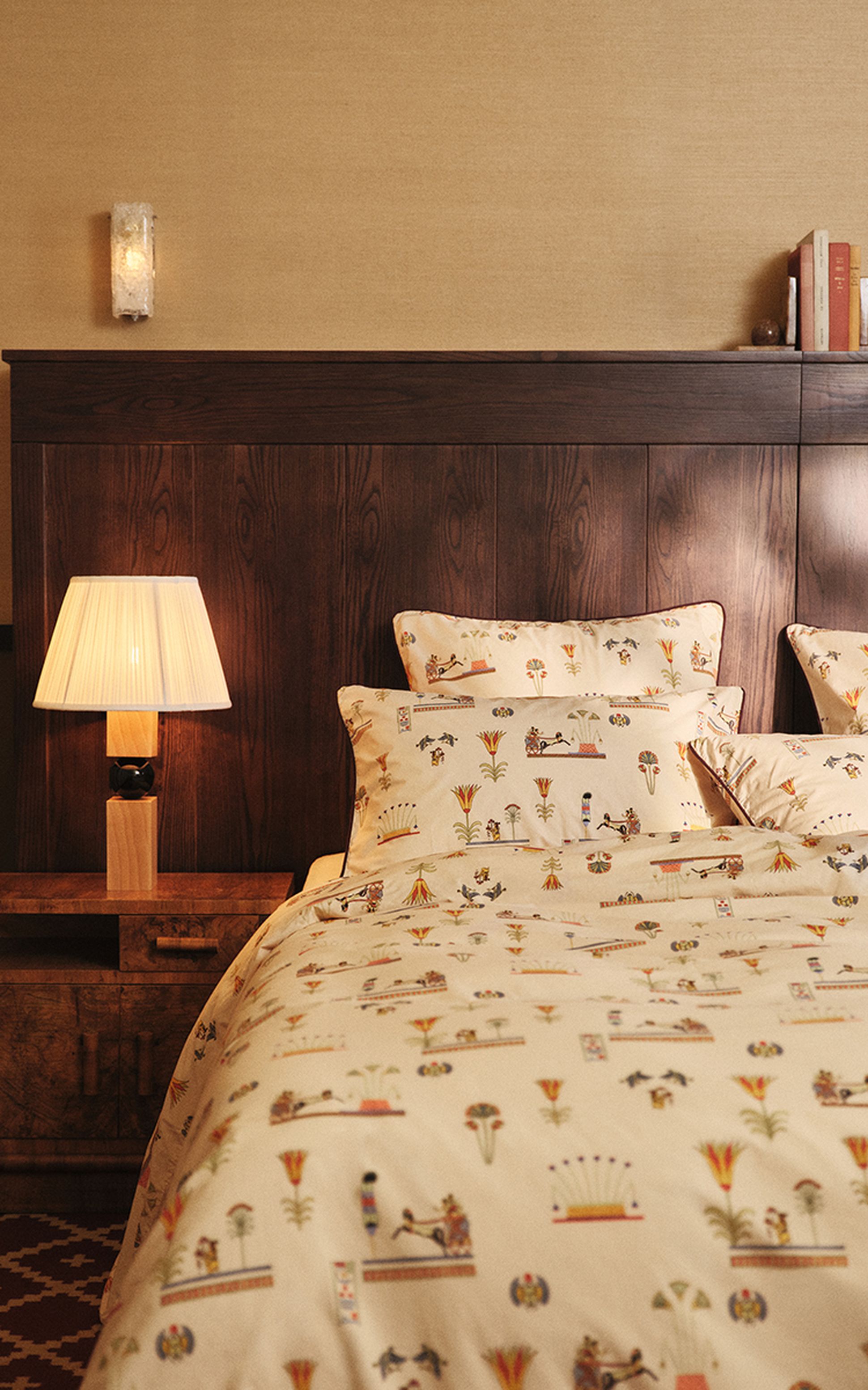Une chambre douillette équipée d'une table de chevet en bois avec une lampe et d'un lit orné d'une parure de lit beige et d'oreillers aux motifs colorés et raffinés.