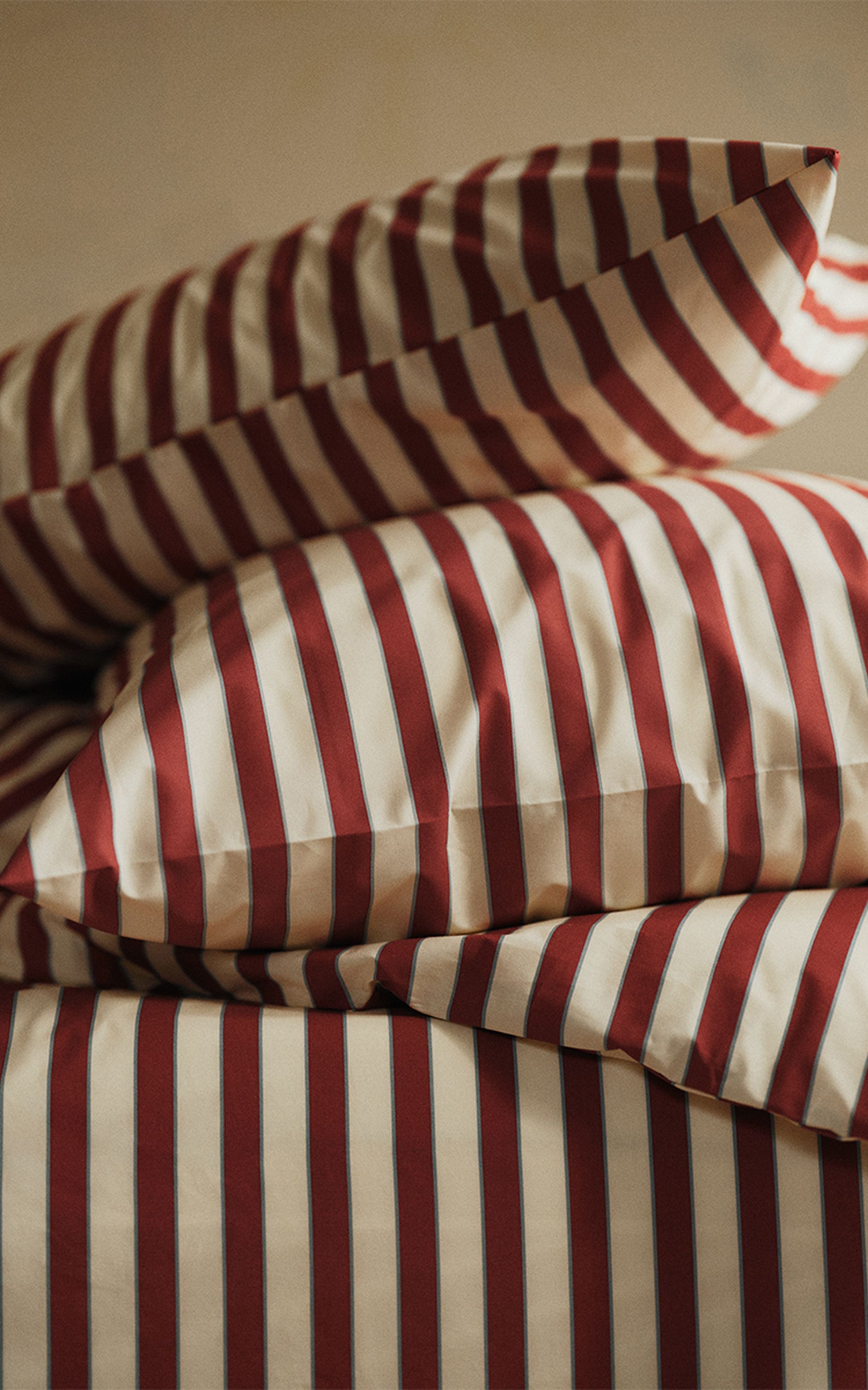 Des oreillers et des coussins rayés rouges et blancs empilés sur un lit, créant une ambiance chaleureuse et accueillante.
