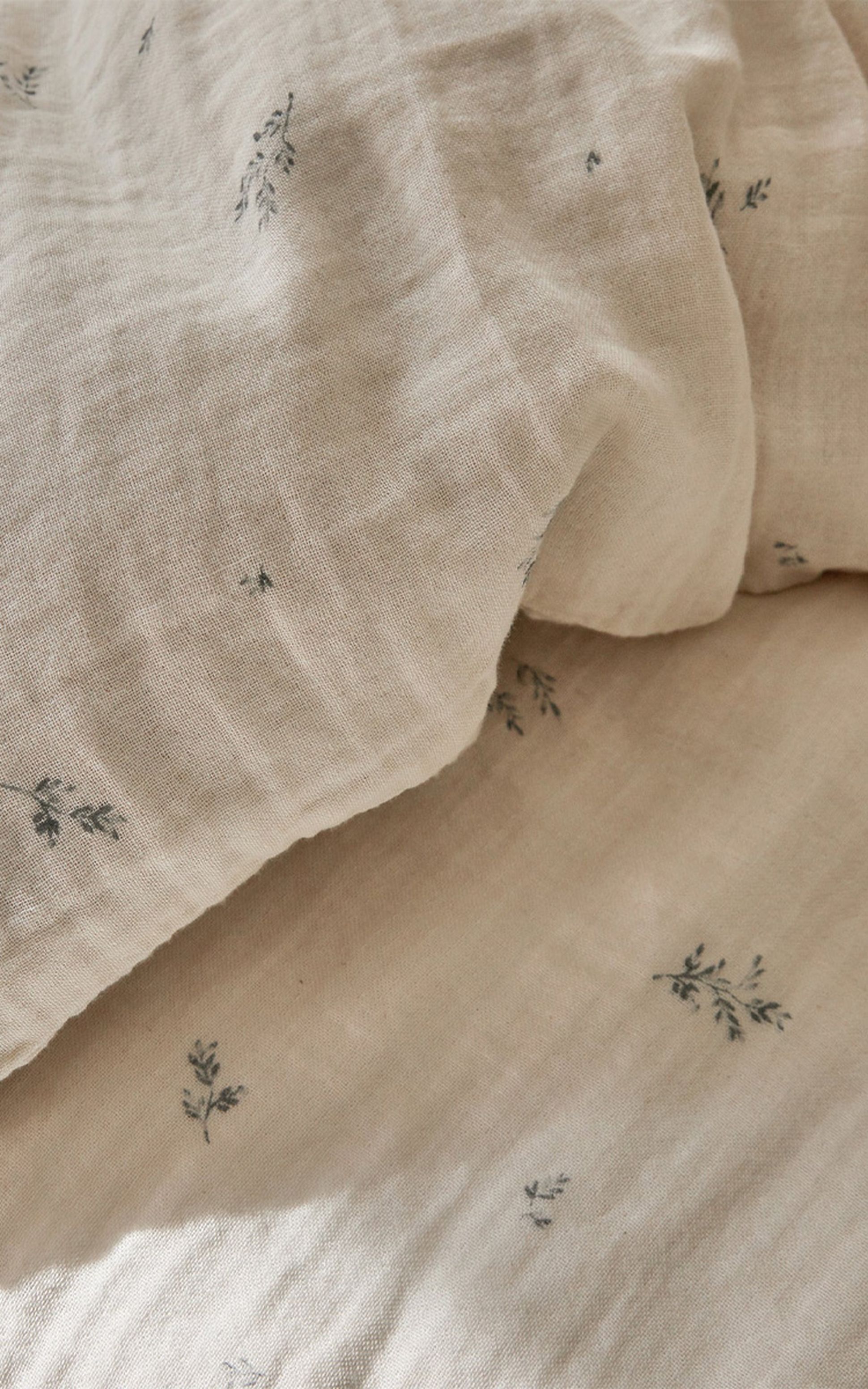 Tissu de couleur crème avec de petits motifs floraux délicats dispersés un peu partout. La texture semble douce et légèrement froissée.