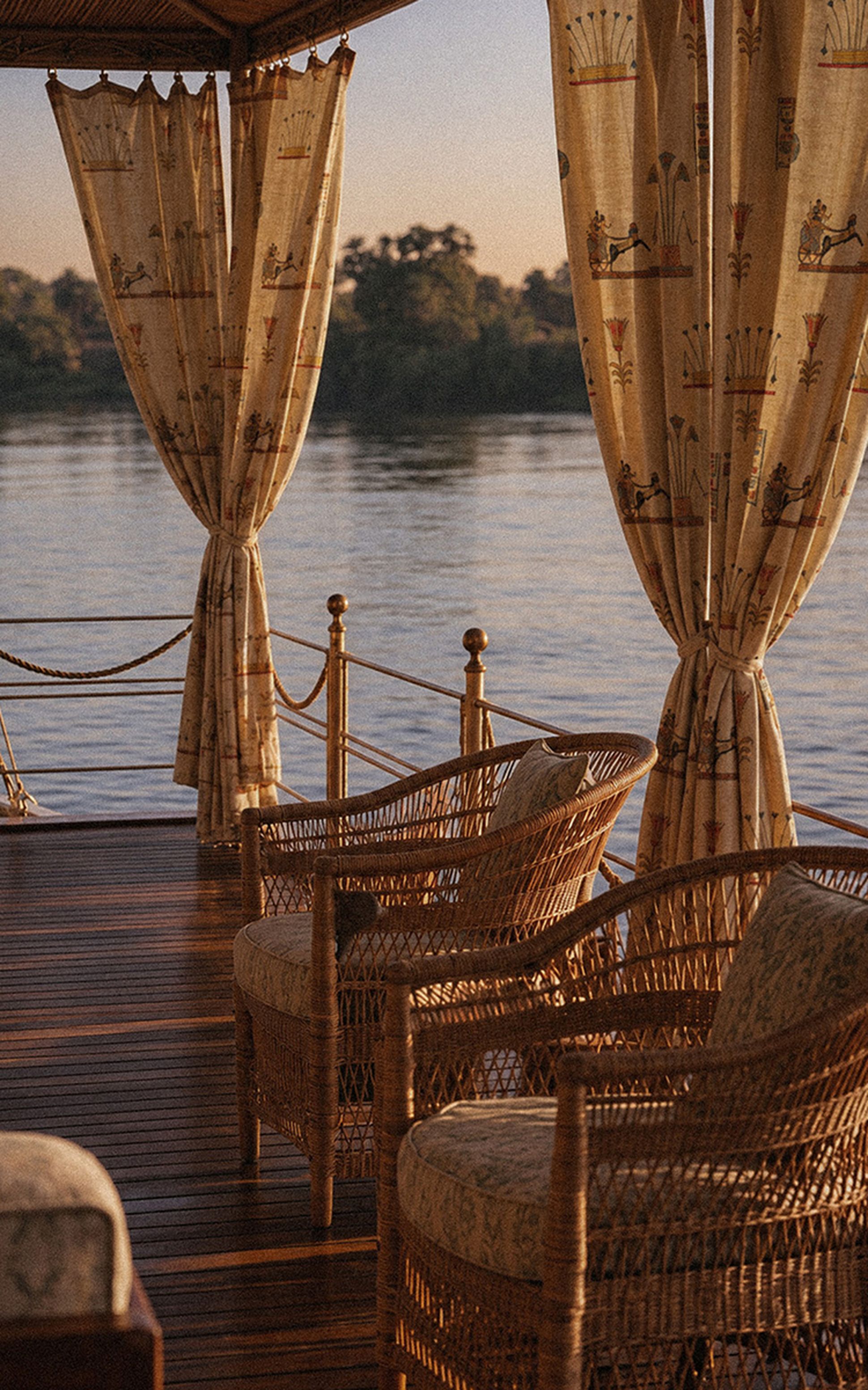 Wicker chairs on a wooden deck overlooking a river at sunset, with decorative curtains framing the view.