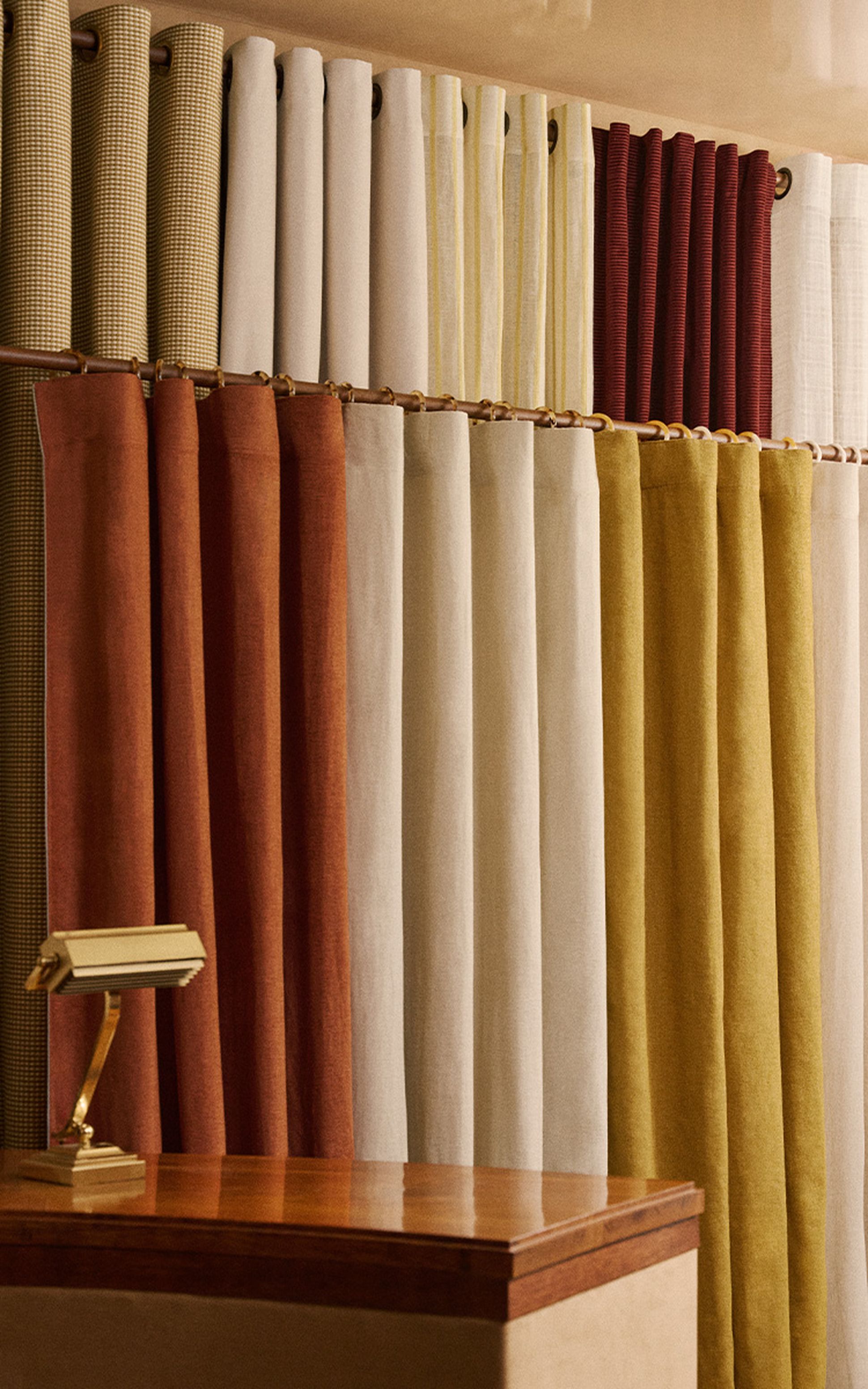 Une variété de rideaux en tissu rouge, beige, jaune et à motifs sont suspendus à une tringle dans la vitrine d'un magasin.