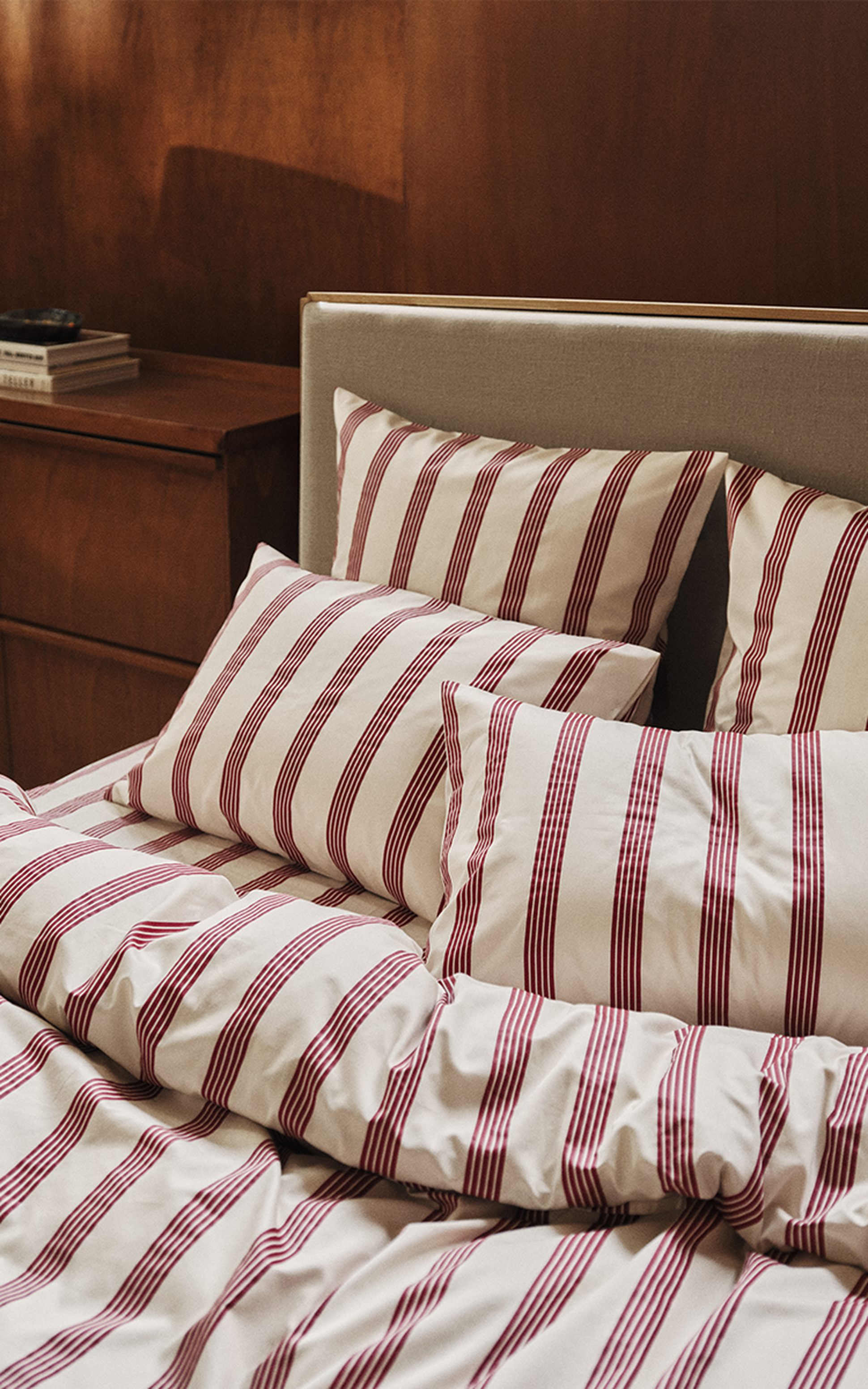 Linge de lit rayé de bordeaux et de blanc sur un lit agrémenté de plusieurs oreillers et d'une couette, dans une chambre à l'ambiance chaleureuse.