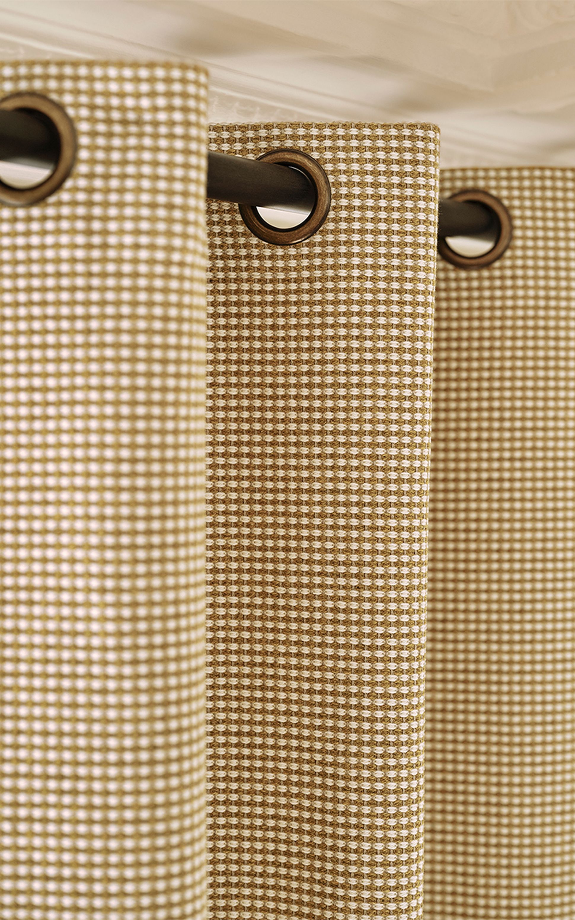 Gros plan sur des rideaux à carreaux beiges et blancs, dotés d'œillets ronds noirs, tombant en plis qui mettent en valeur la texture et le motif du tissu.