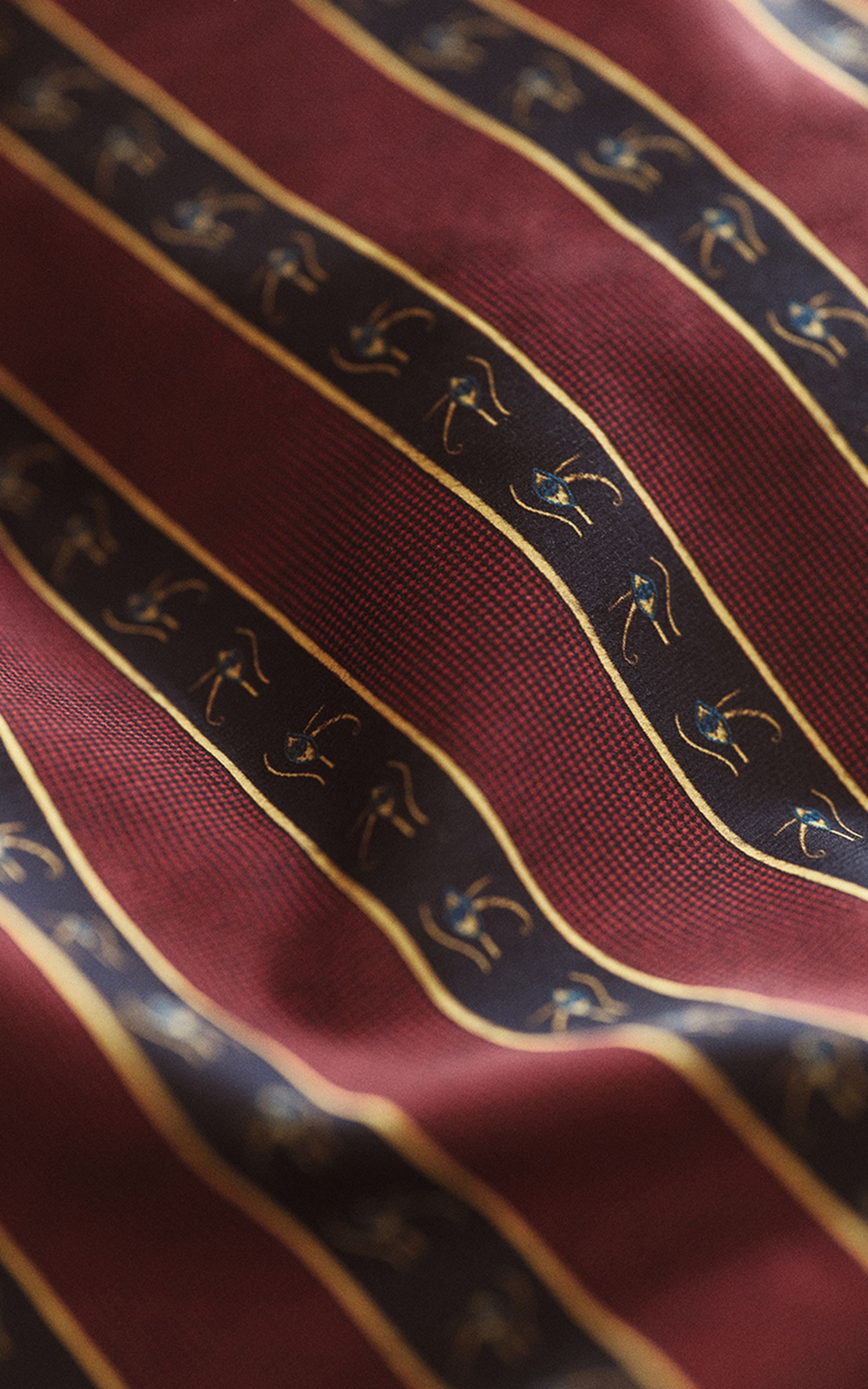 Close-up of a maroon fabric with diagonal black stripes featuring gold Egyptian Eye of Horus motifs.