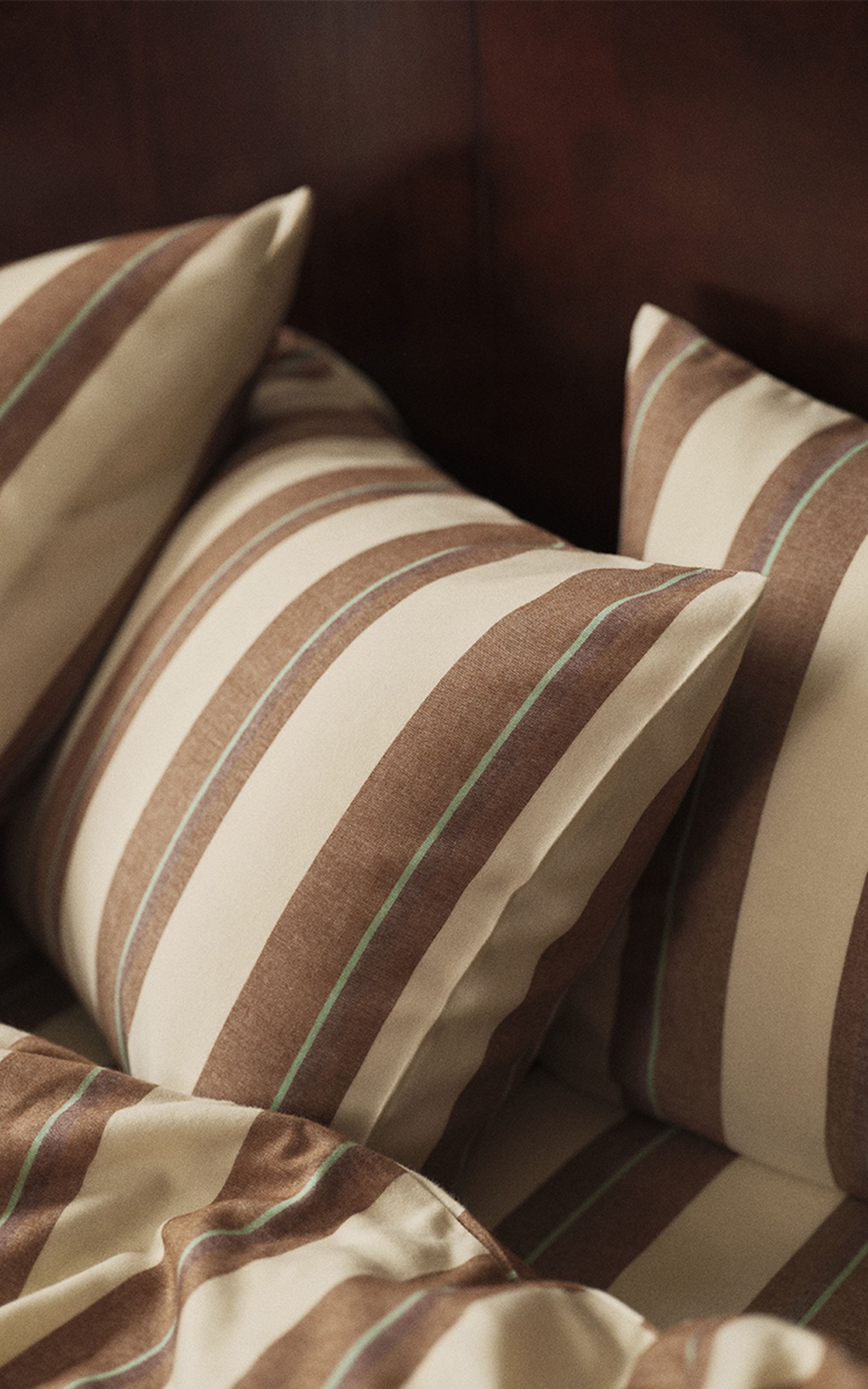 Gros plan sur un lit orné d'oreillers et d'une couverture rayés de marron et de beige, devant une tête de lit en bois foncé.