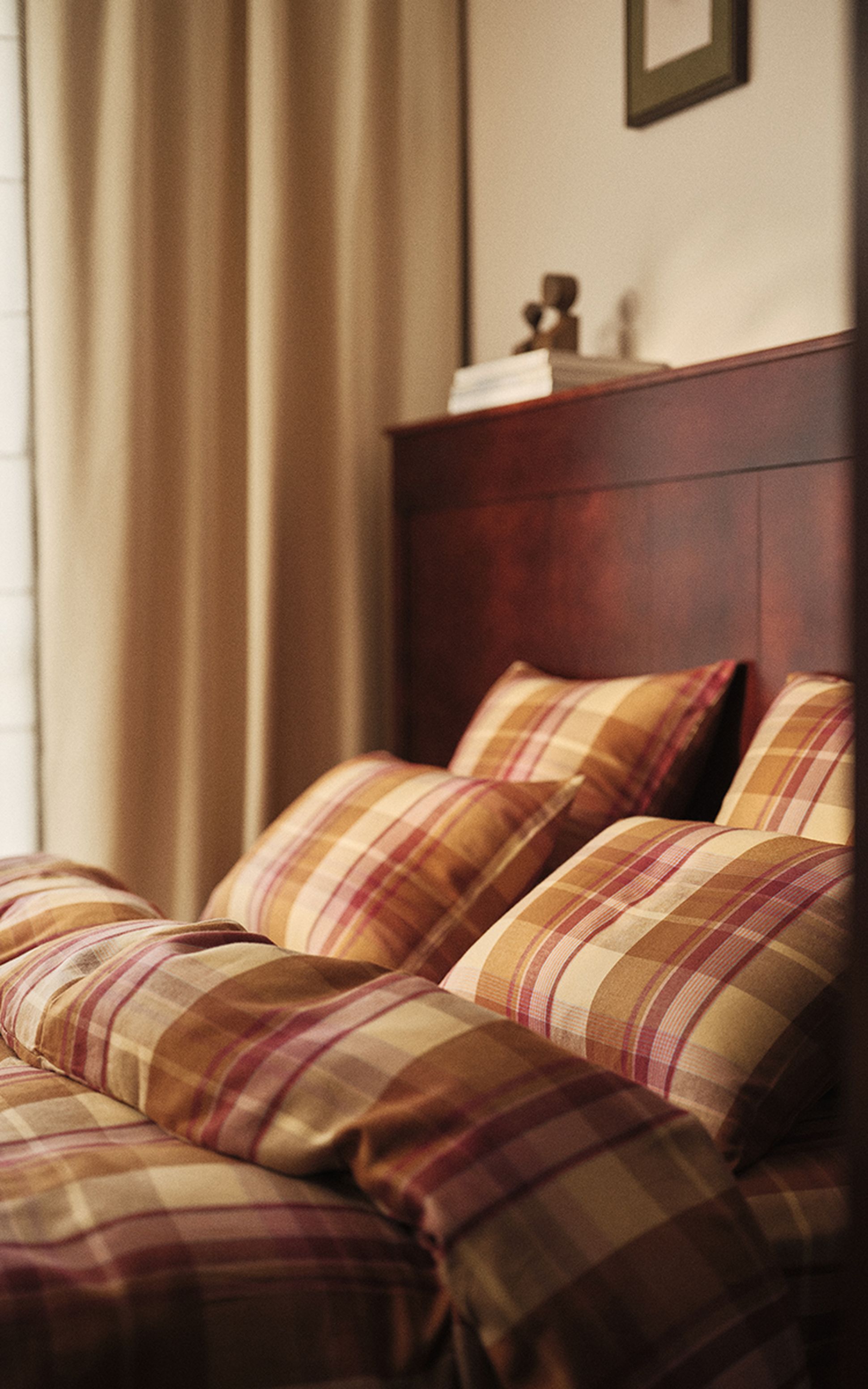 Une chambre douillette avec un ensemble de literie à carreaux, une tête de lit en bois et une lumière tamisée provenant d'une fenêtre voisine.