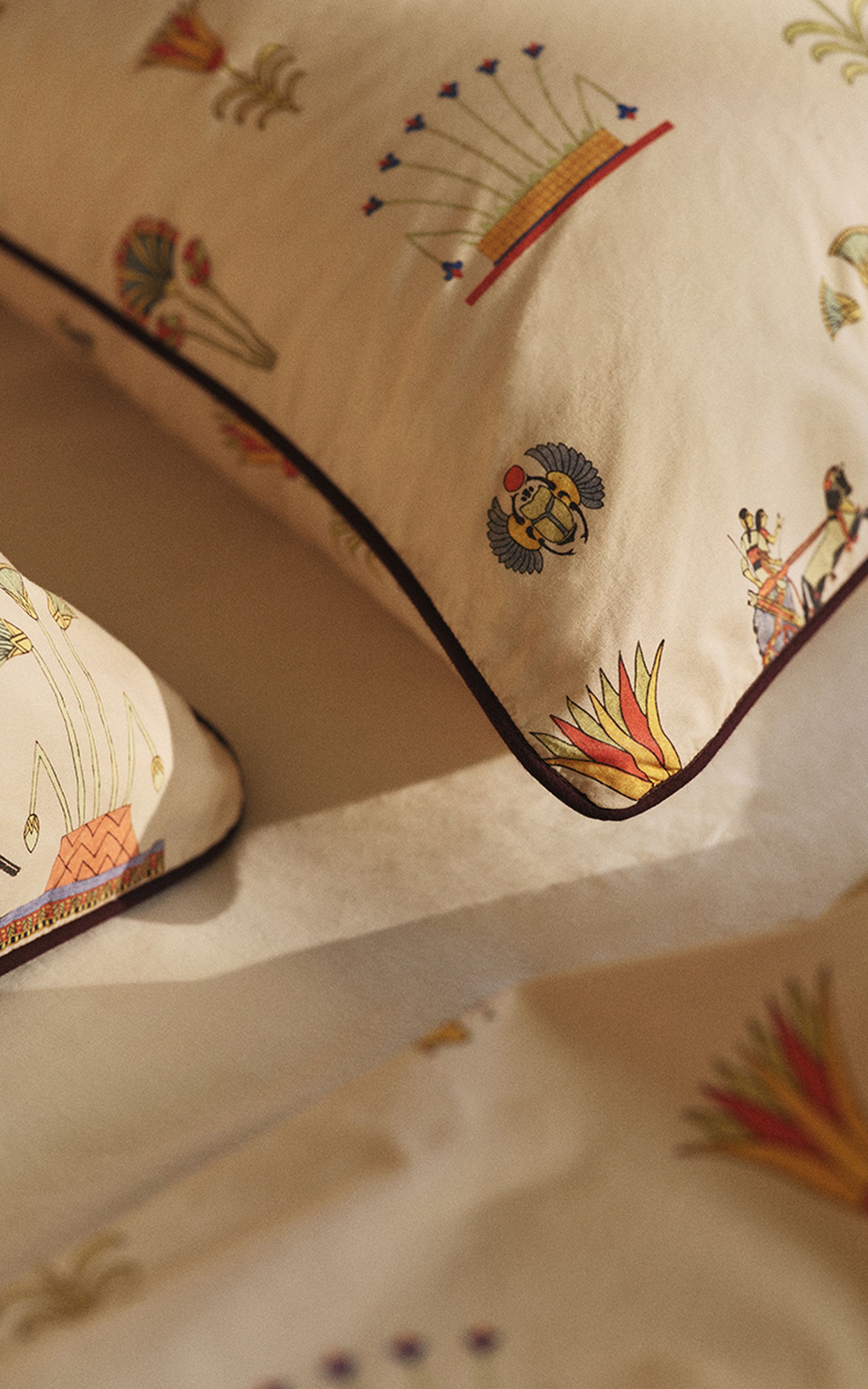 Cream-colored pillowcases with Egyptian-inspired patterns, featuring scarabs and abstract motifs, on a matching sheet set.