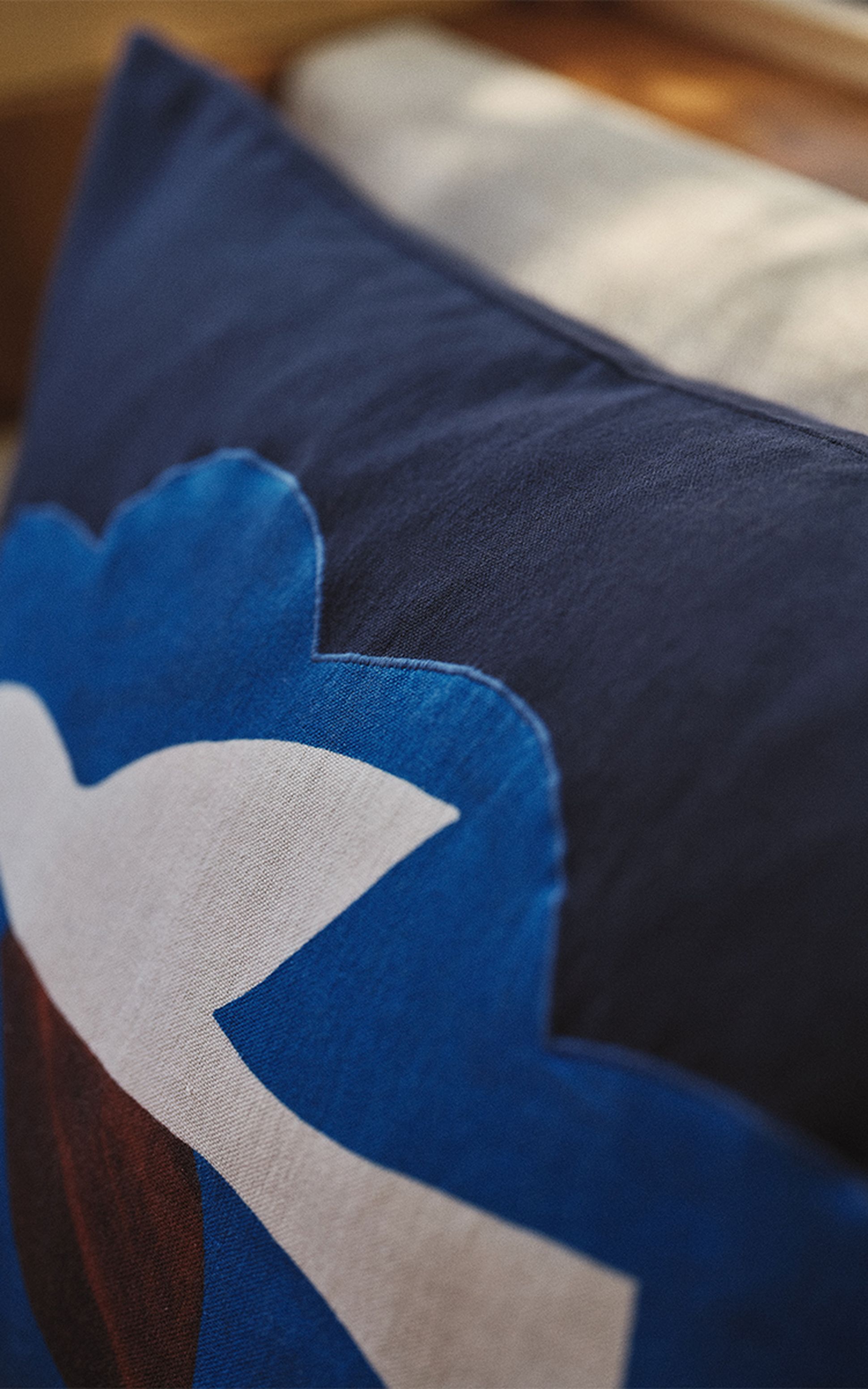 Gros plan sur un coussin recouvert d'une housse bleu foncé, orné d'un motif abstrait dans les tons de bleu, blanc et marron, posé sur un canapé.