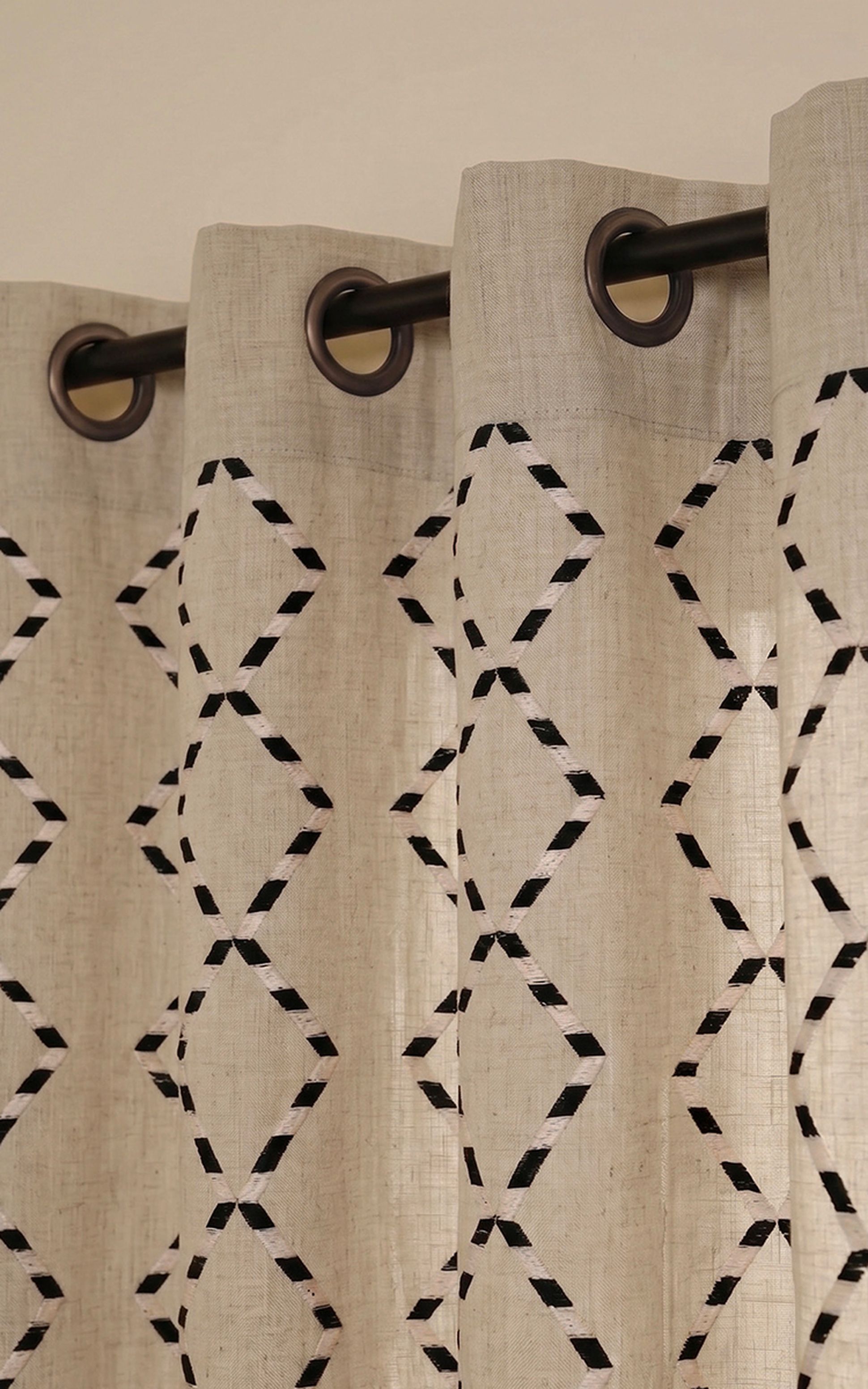 Des rideaux beiges à motifs de losanges noirs et blancs, suspendus à une tringle à l'aide d'œillets métalliques.