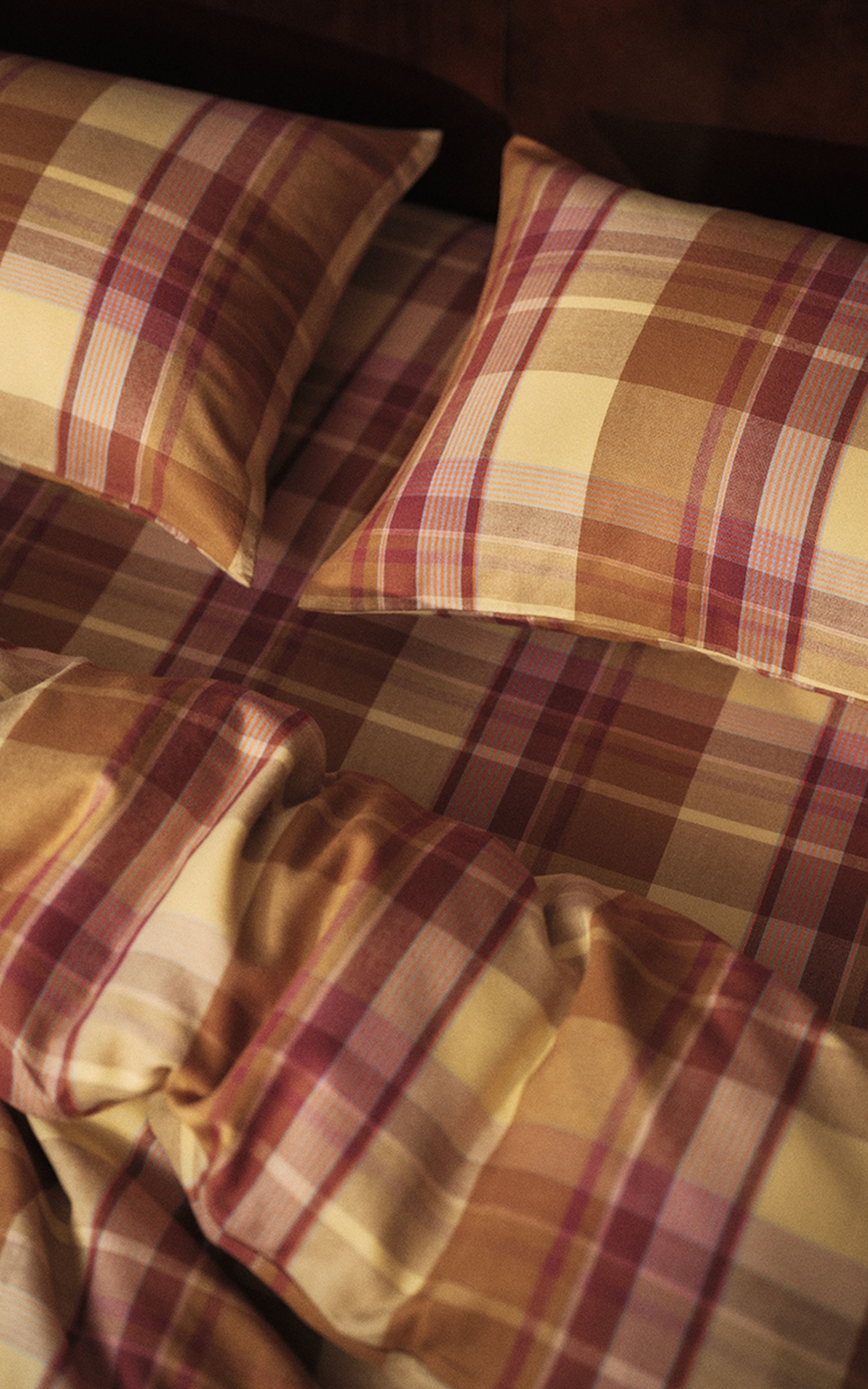 Ensemble de literie à carreaux dans les tons rouge, beige et jaune, agrémenté de deux oreillers assortis posés sur le lit, créant une ambiance chaleureuse et douillette.