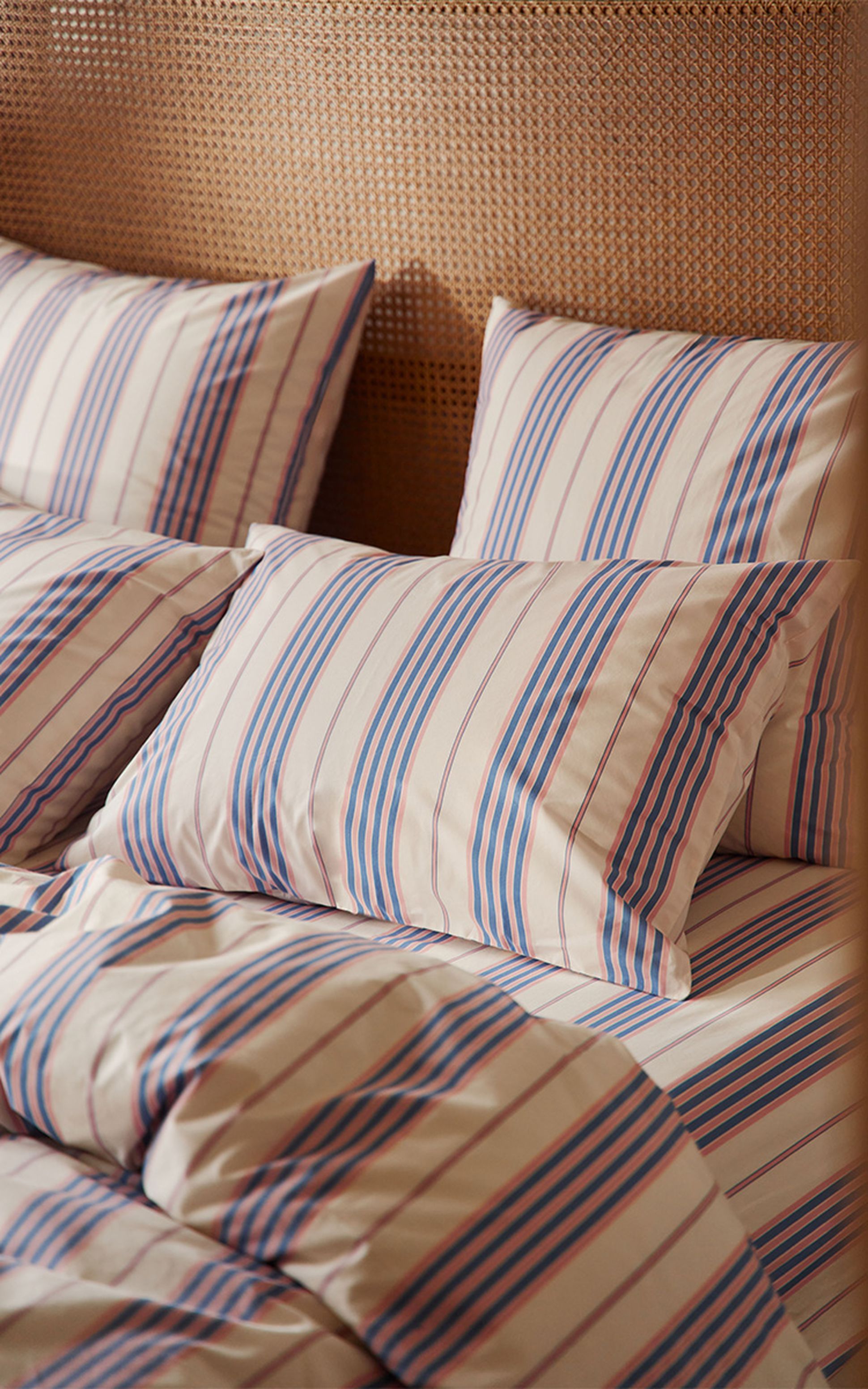 Lit avec oreillers et couette à rayures bleues, rouges et blanches, sur fond de tête de lit tissée texturée.