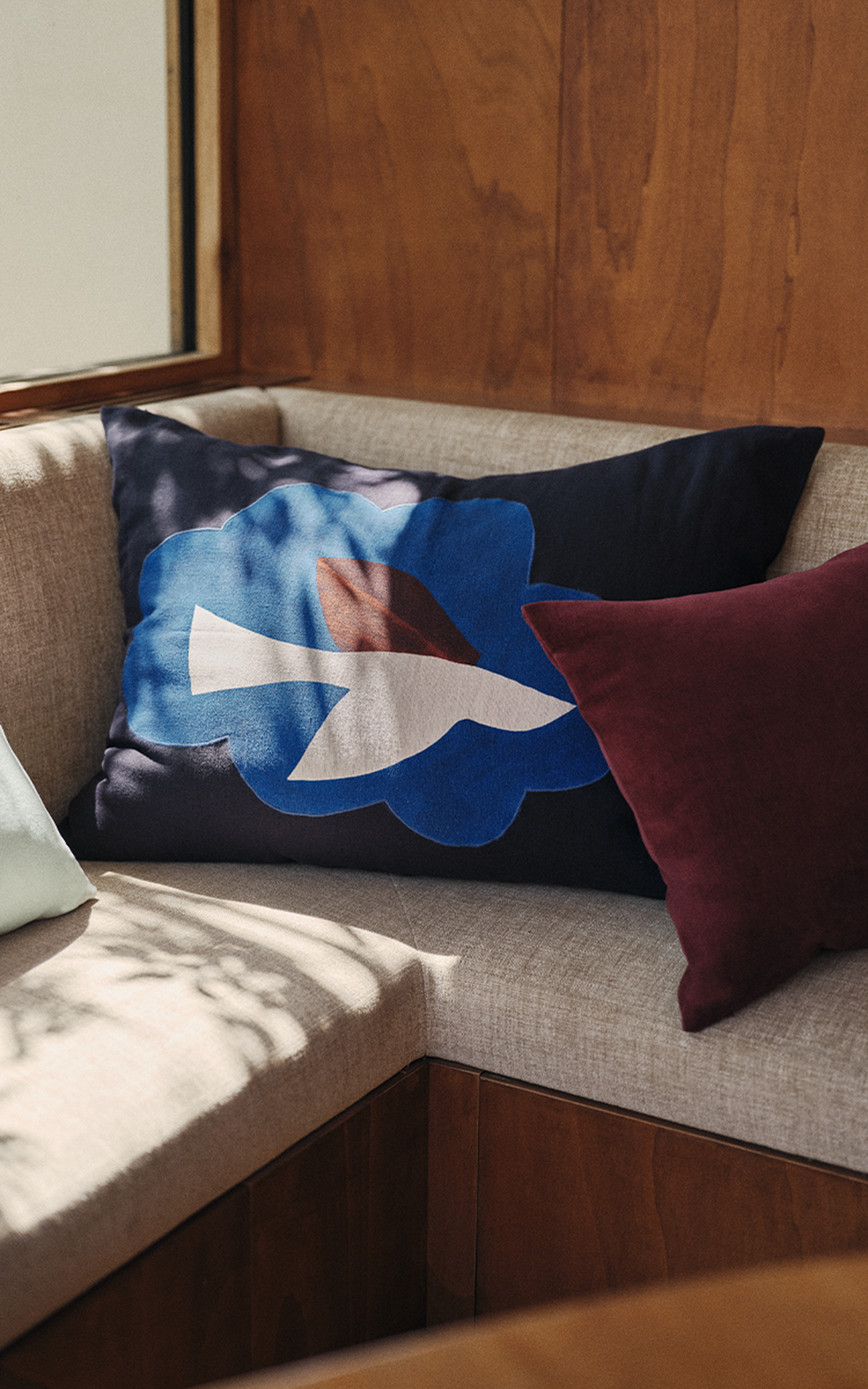 Un coin salon chaleureux, agrémenté de coussins décoratifs aux motifs abstraits dans les tons de bleu, blanc et rouge, sur fond de mur en bois.