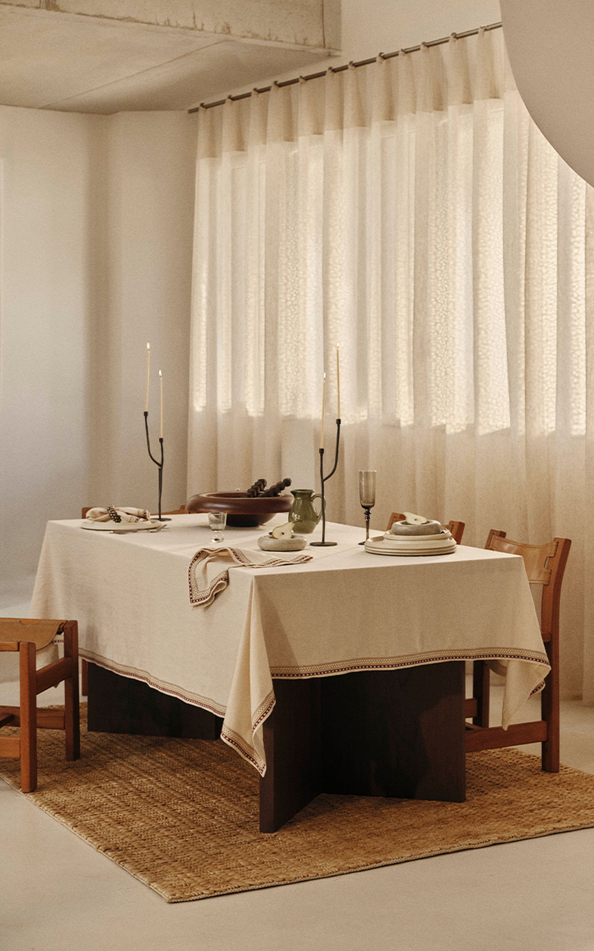 Une salle à manger minimaliste avec une table dressée pour deux, agrémentée de grandes bougies, d'une vaisselle sobre et de tons neutres, baignée d'une douce lumière naturelle.