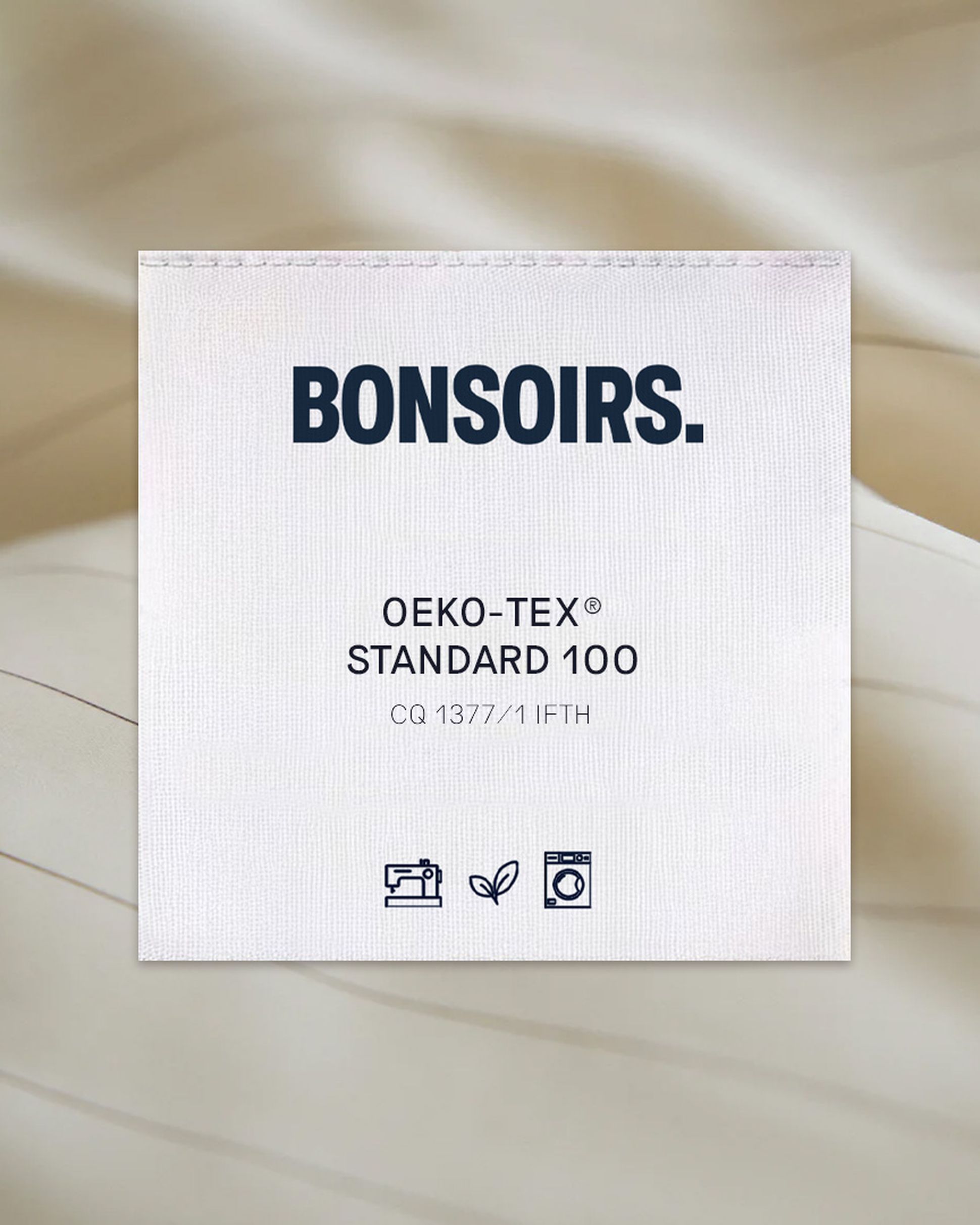 Étiquette en tissu portant la mention « BONSOIRS », « OEKO-TEX STANDARD 100 », des symboles indiquant les consignes de lavage et le respect de l'environnement, ainsi qu'un code d'identification.