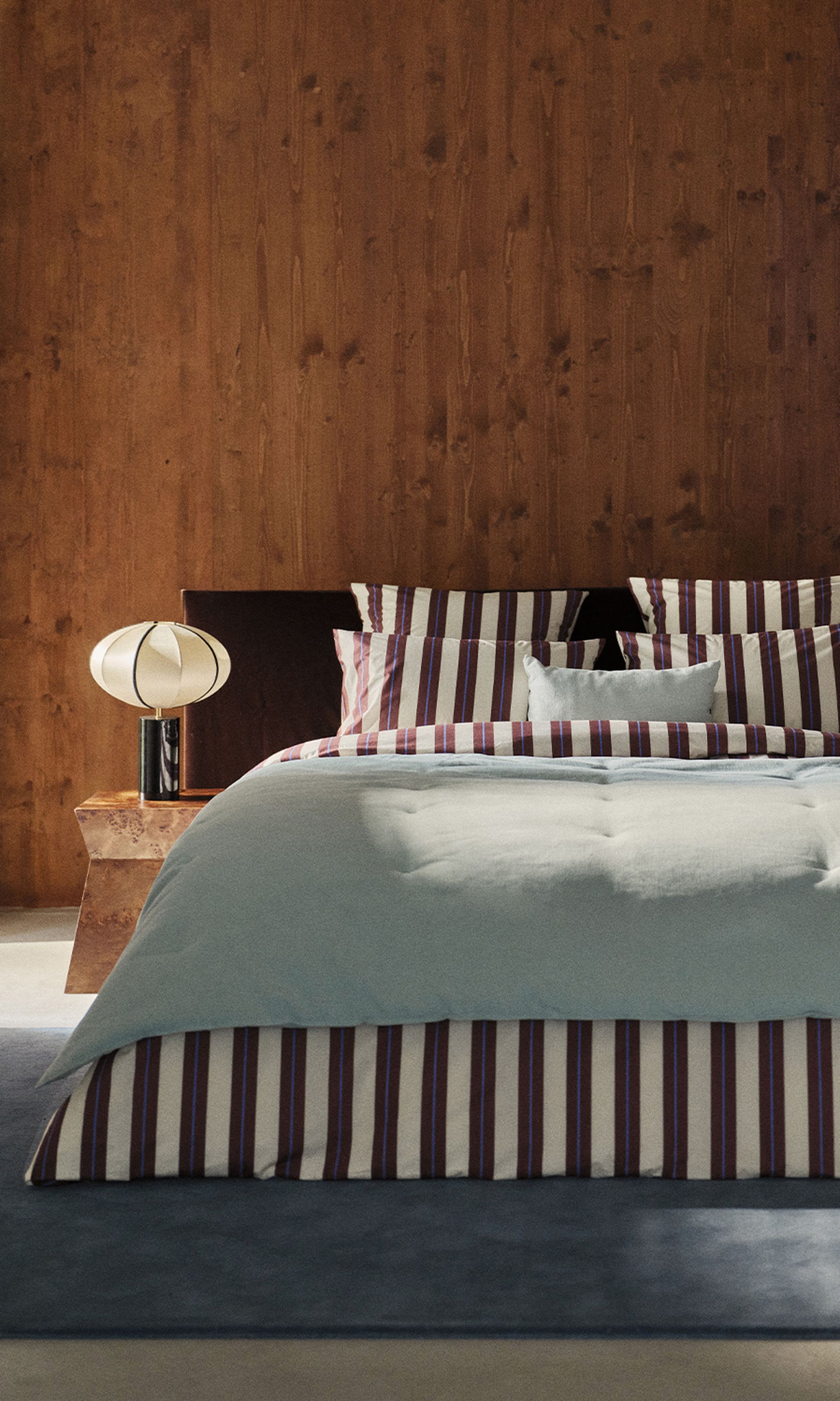 Une chambre moderne avec un mur en bois, une parure de lit rayée rouge et blanche et des lampes rondes posées sur des tables de chevet rustiques.