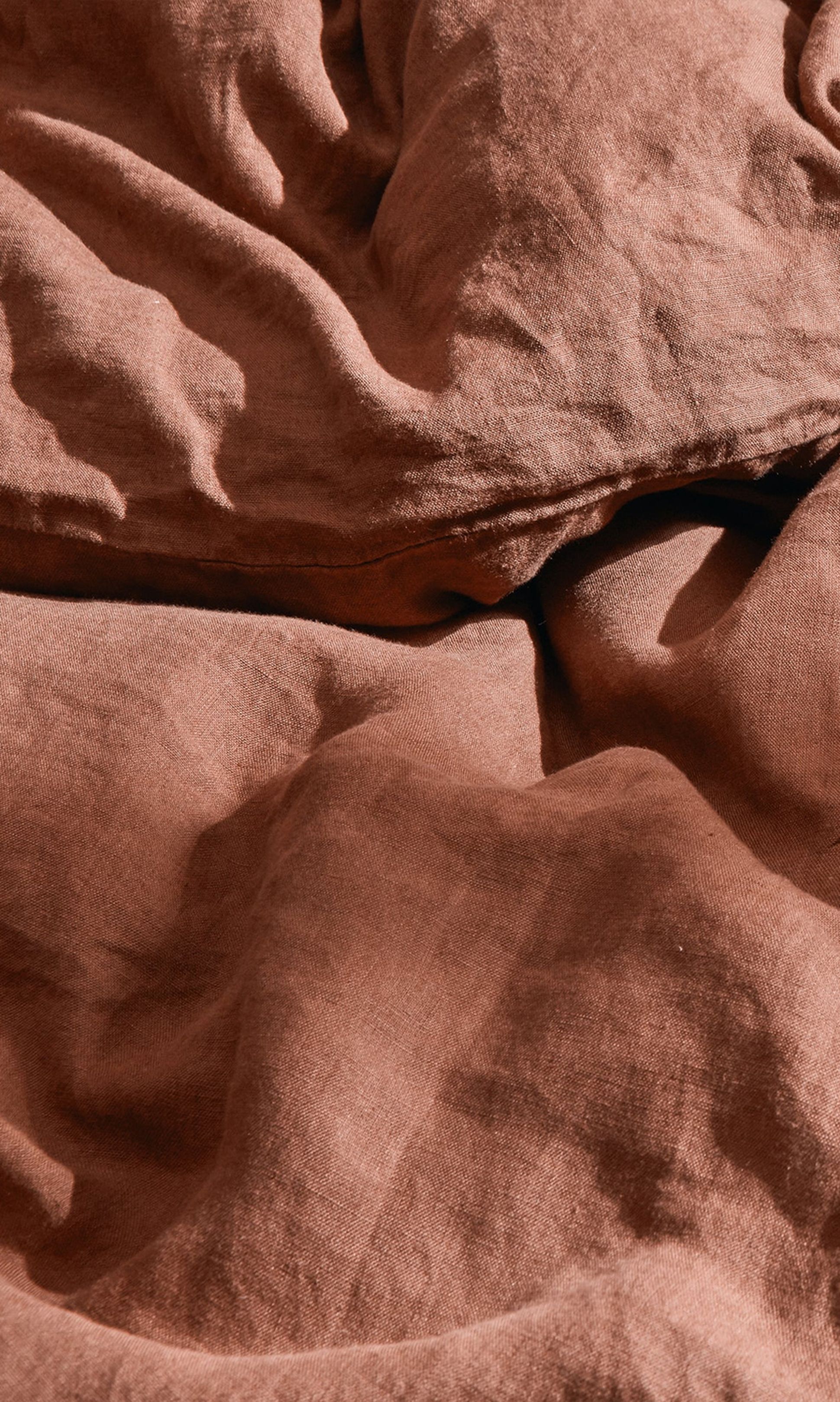 Tissu froissé de couleur rouille, présentant des plis et des plis visibles qui créent une surface texturée.