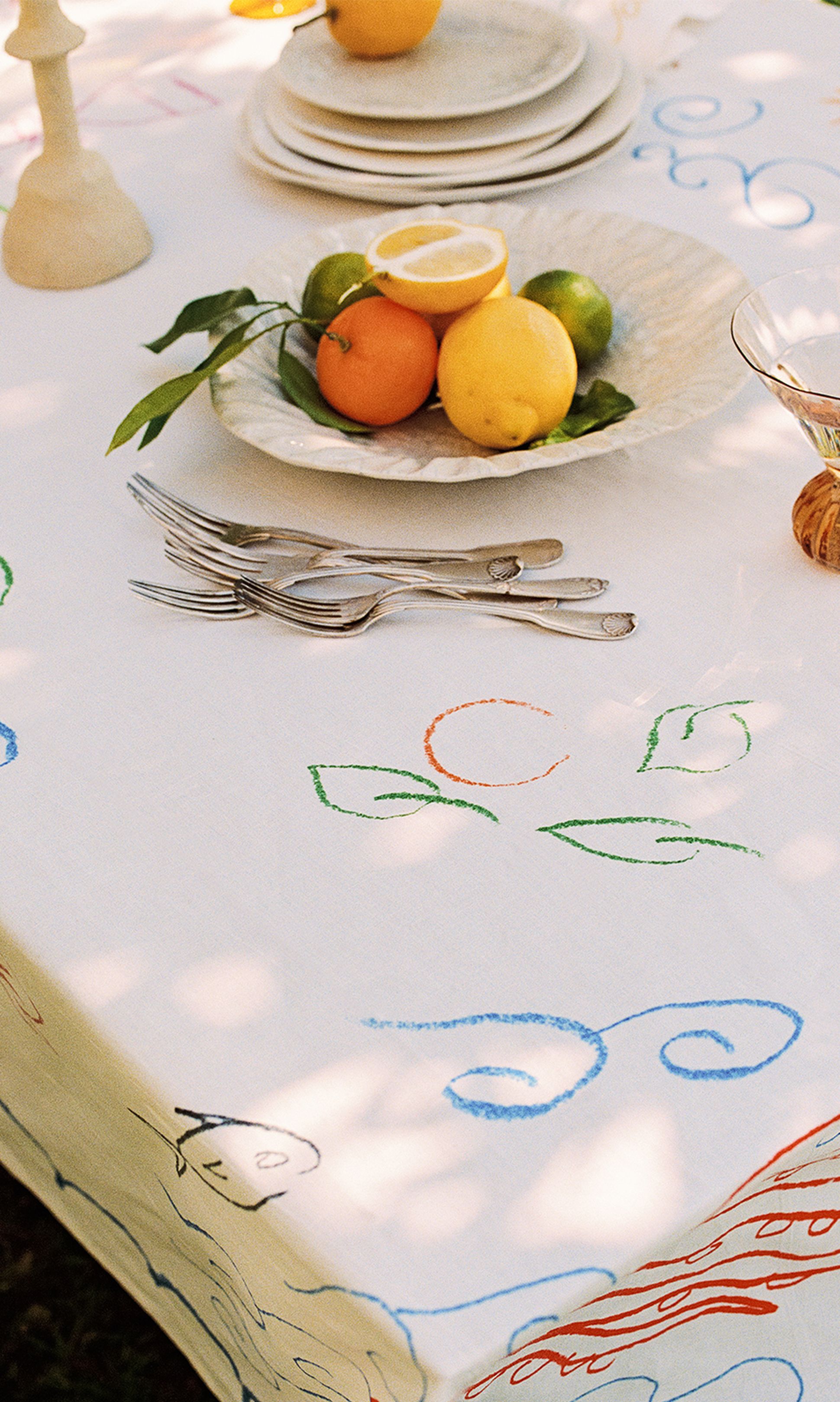 Une table ornée de broderies colorées est dressée d'une assiette d'agrumes, d'assiettes empilées et de fourchettes, créant ainsi une ambiance en plein air pleine de vie.