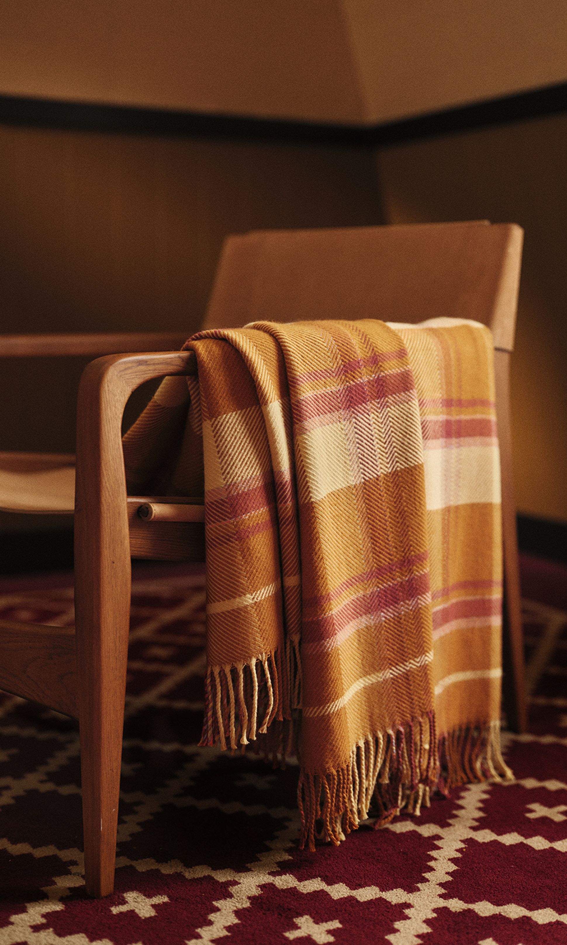 Une chaise en bois recouverte d'une couverture à carreaux aux couleurs chaudes, posée sur un tapis rouge à motifs dans une pièce chaleureuse.