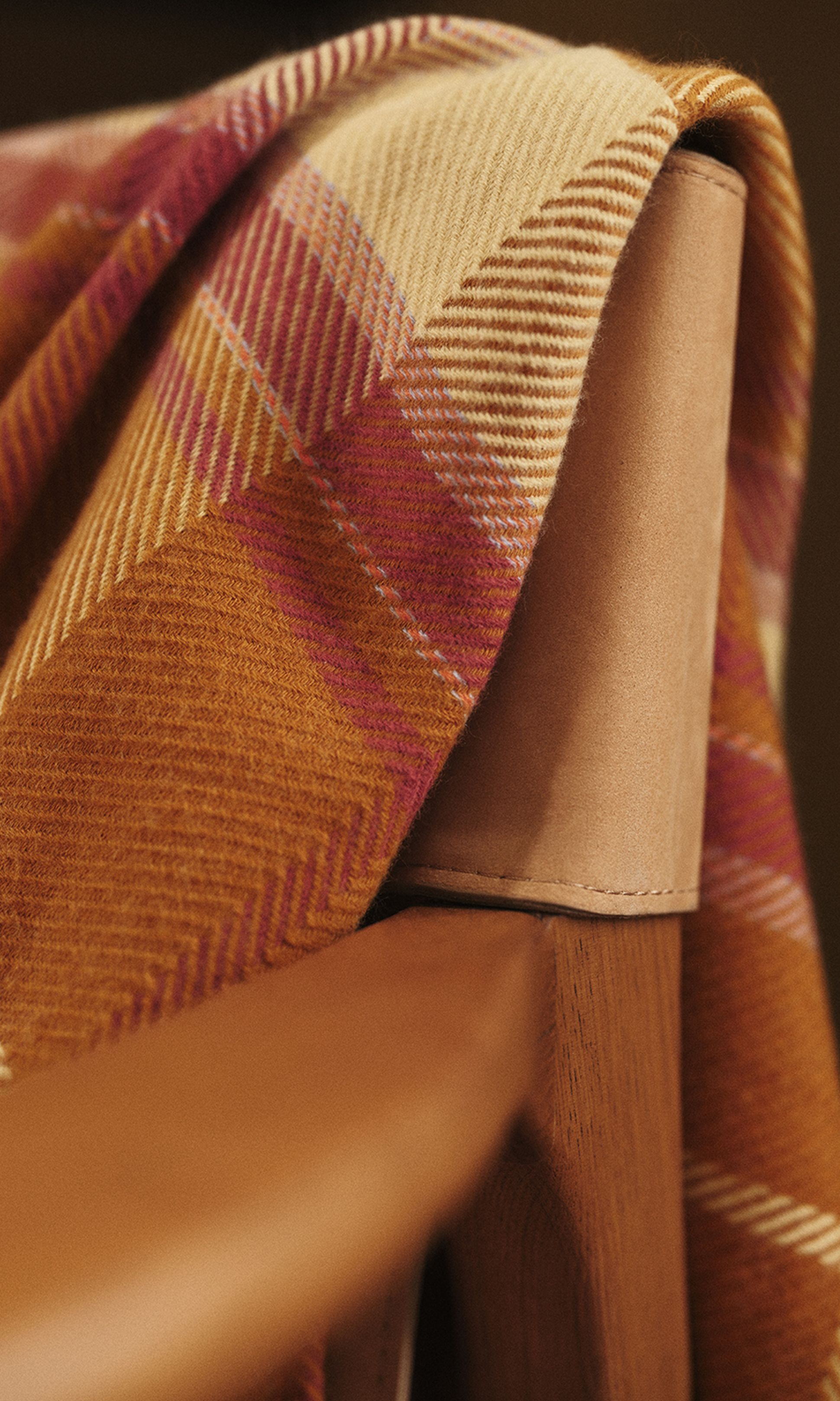 Un tissu à carreaux dans les tons orange et rose est drapé sur le dossier d'une chaise en bois.