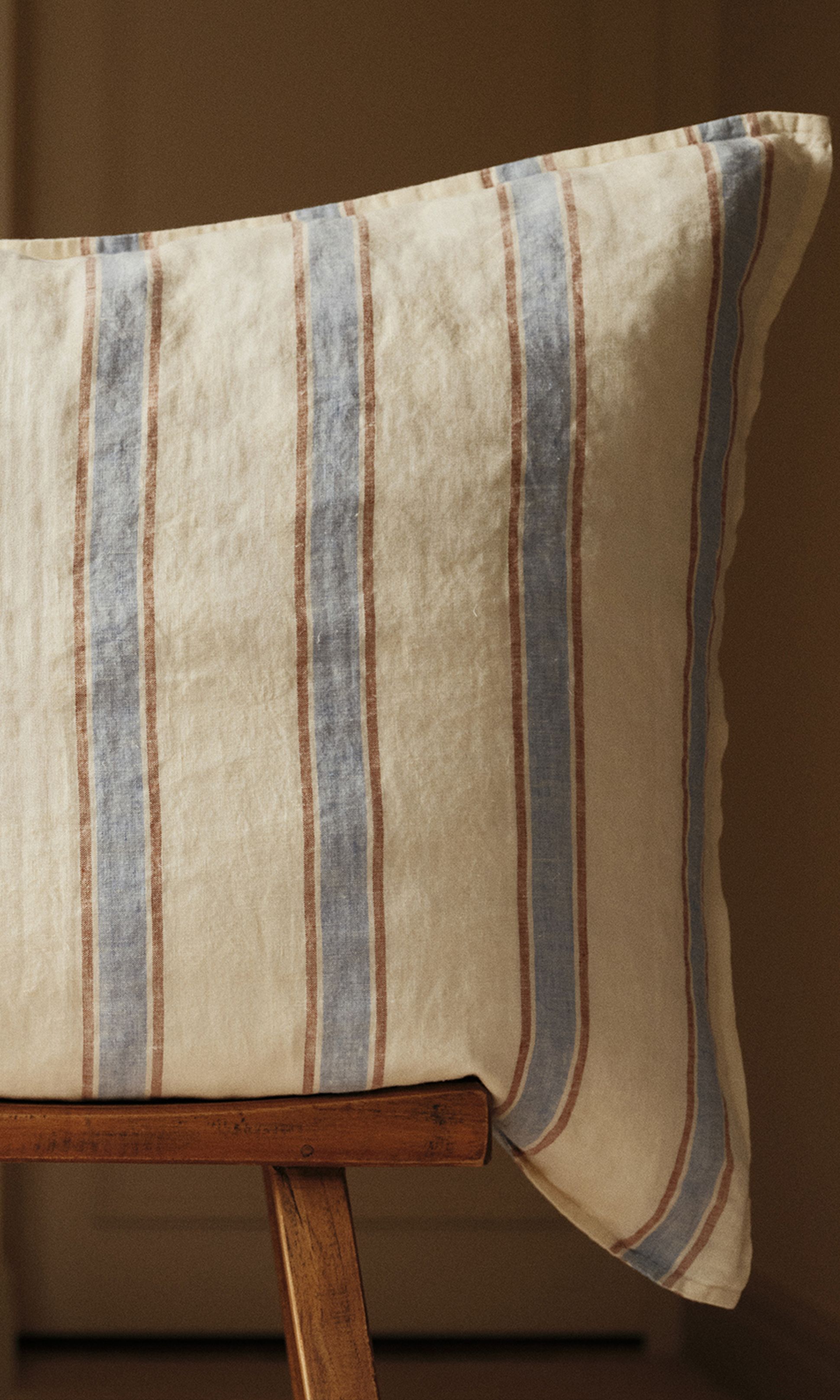 Un coussin à rayures verticales bleues et marron posé sur une chaise en bois, sur fond neutre et chaleureux.