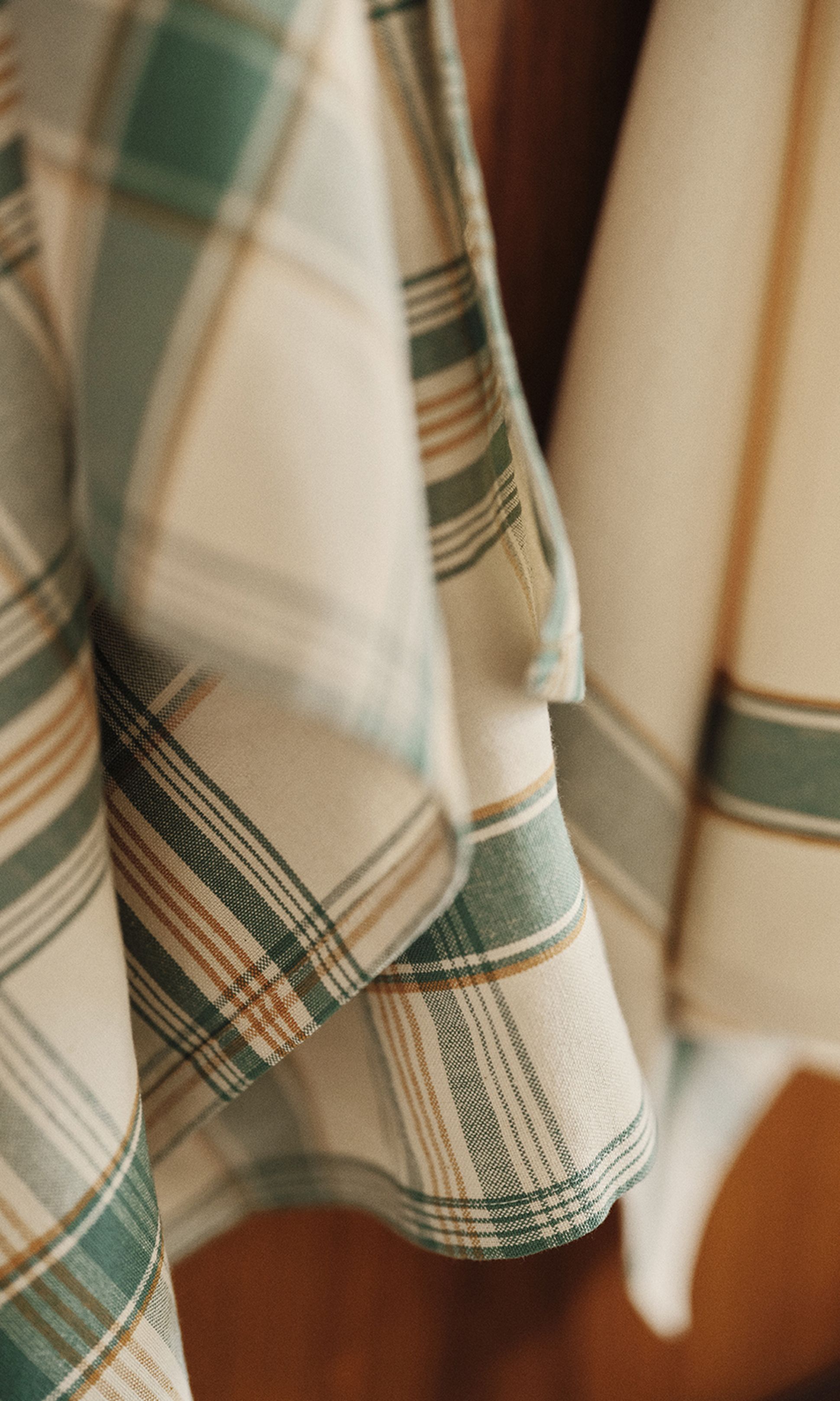Tissu à carreaux, dans des tons de vert, marron et crème, drapé sur une surface en bois.