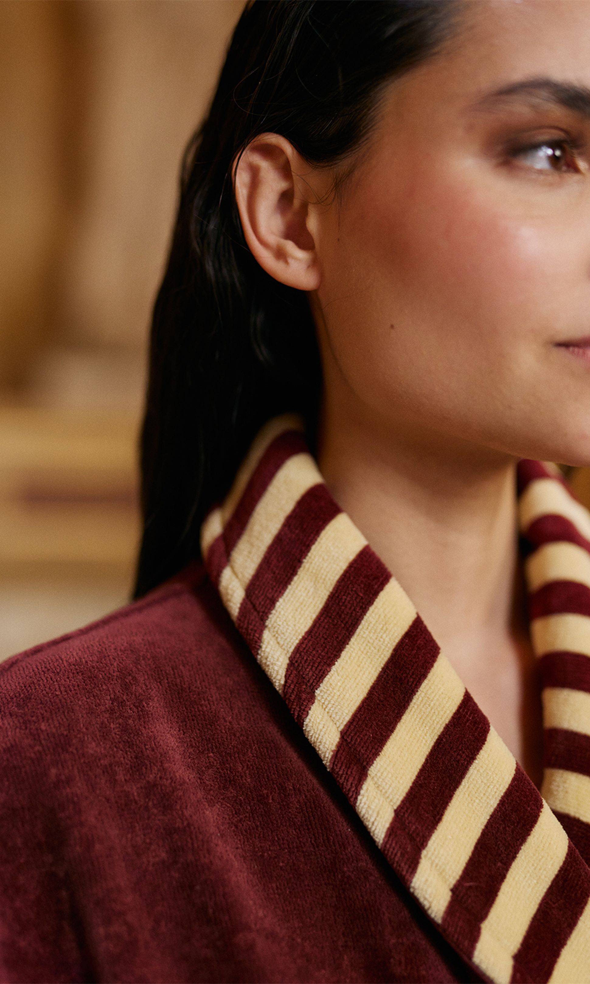 Gros plan sur une personne vêtue d'une robe bordeaux à col rayé marron et beige, mettant en valeur la texture et le motif.