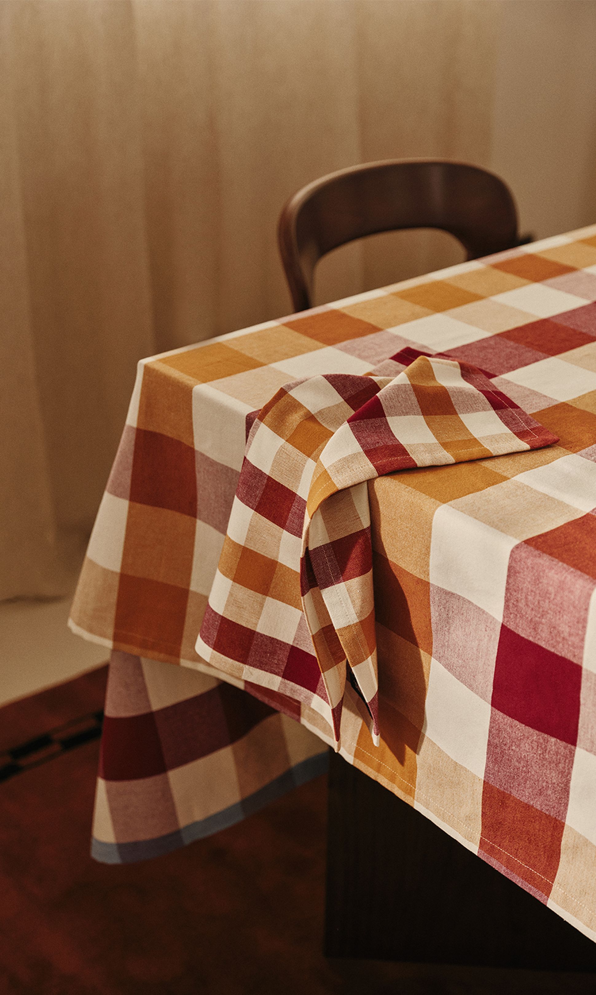 Une nappe à carreaux dans des tons de rouge, d'orange et de beige recouvre une table, avec une serviette pliée assortie.